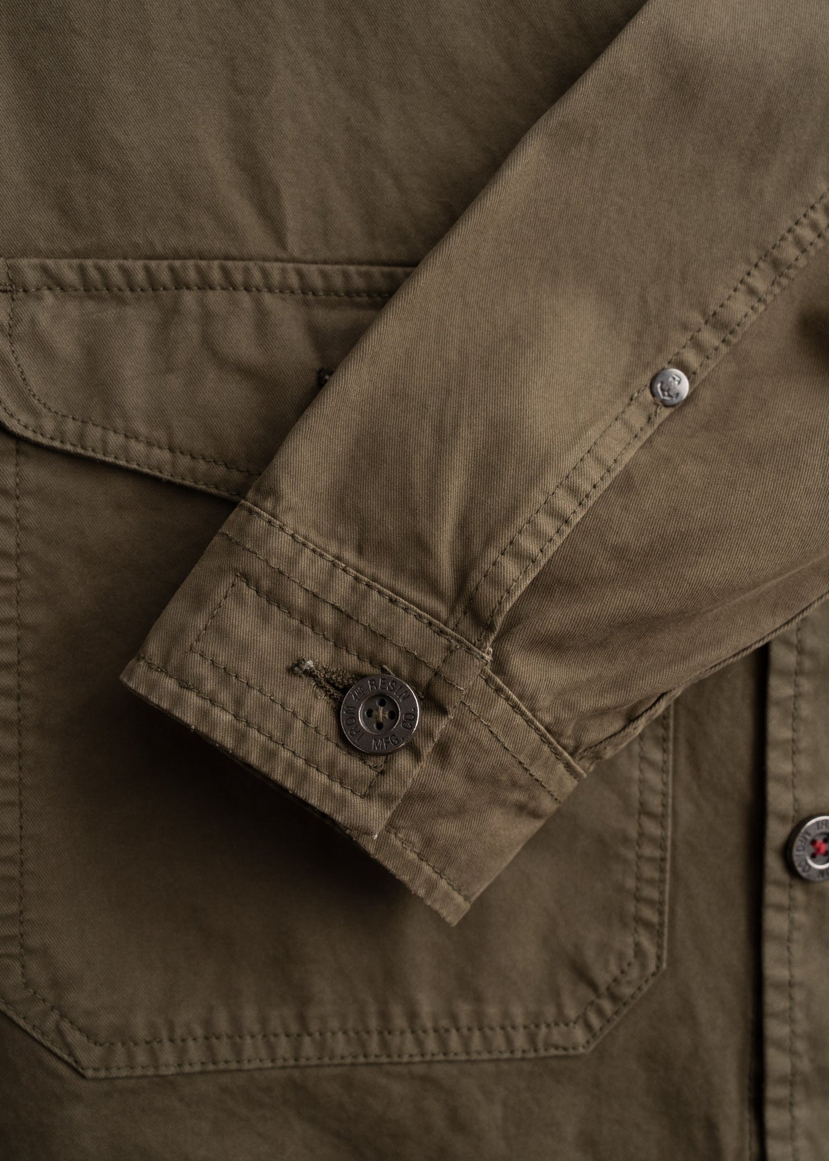 Close-up of a brown jacket sleeve with a buttoned cuff, showcasing detailed stitching and a pocket flap on the fabric.