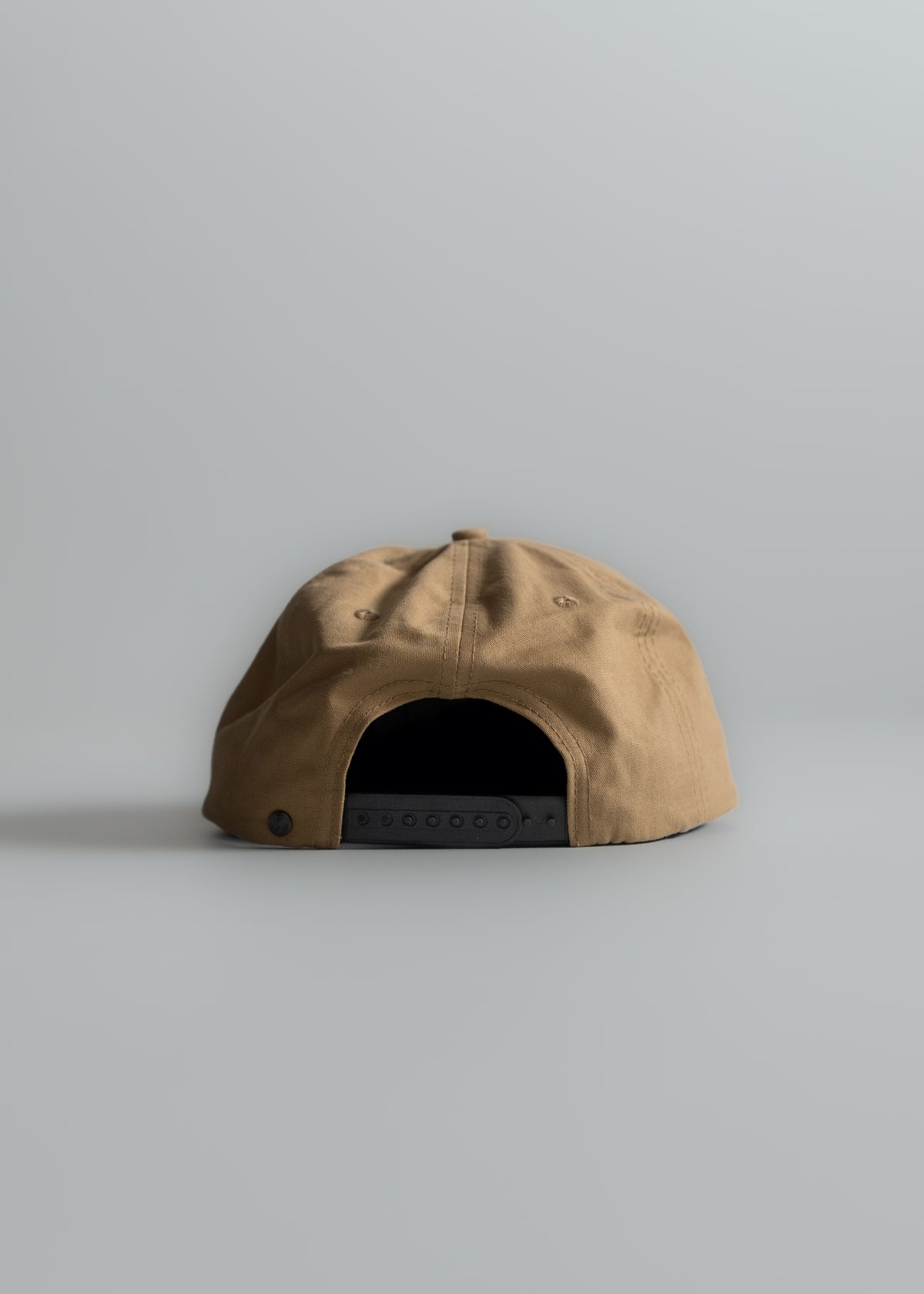 Tan baseball cap with adjustable black strap, viewed from the back, on a plain gray background.
