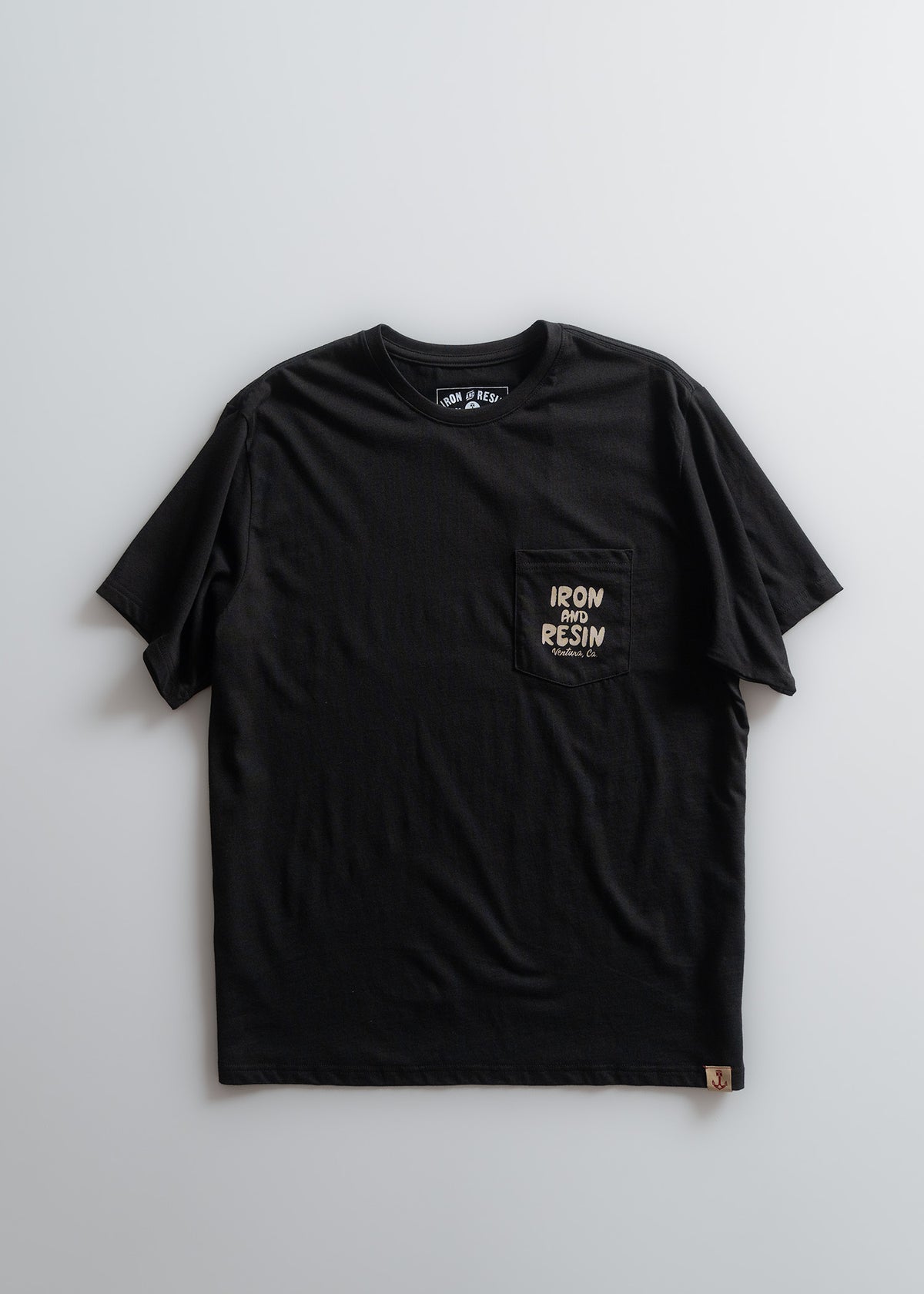 Black "Iron and Resin" t-shirt with pocket logo on light background, showcasing simple design and casual style.