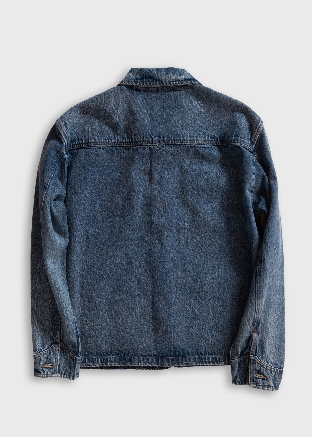 Back view of a classic blue denim jacket with long sleeves, displayed on a plain white background, showcasing its simple design.