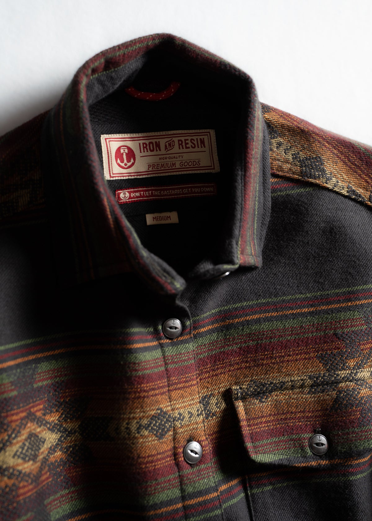Plaid shirt with Iron and Resin label, featuring earthy tones and metal buttons, highlighting premium craftsmanship and style.