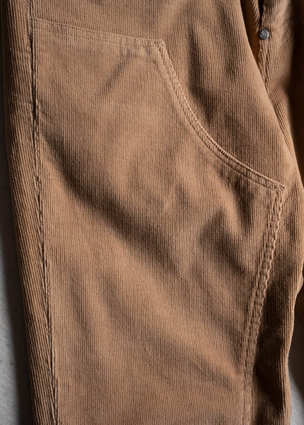Close-up of brown corduroy pants showing texture and stitching detail, highlighting the pocket and button on the right side.
