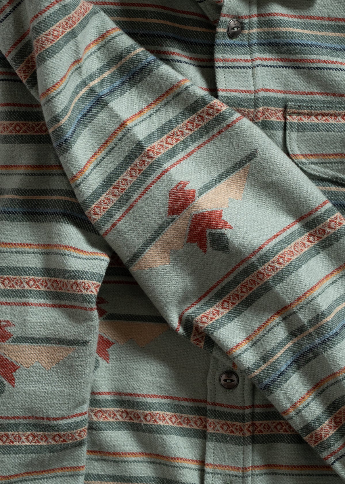 Close-up of a patterned shirt with green, red, and beige stripes and geometric designs, highlighting its texture and buttons.