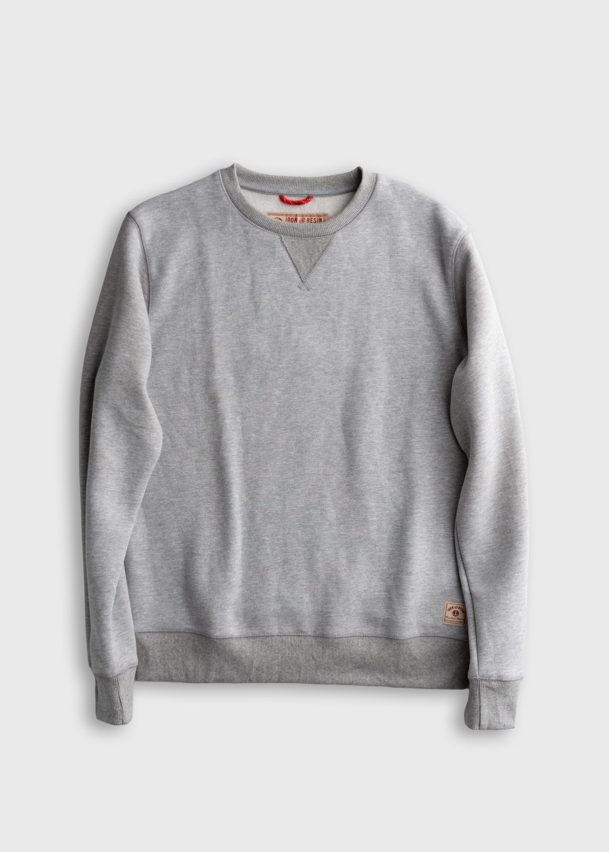 Gray crewneck sweatshirt with ribbed cuffs and hem, featuring a small logo patch on the lower side against a plain background.