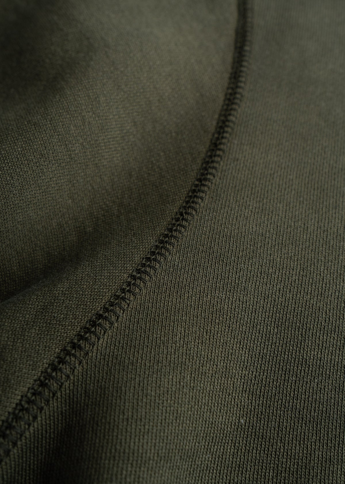 Close-up of olive green fabric with a prominent seam running diagonally, showcasing texture and stitching detail.
