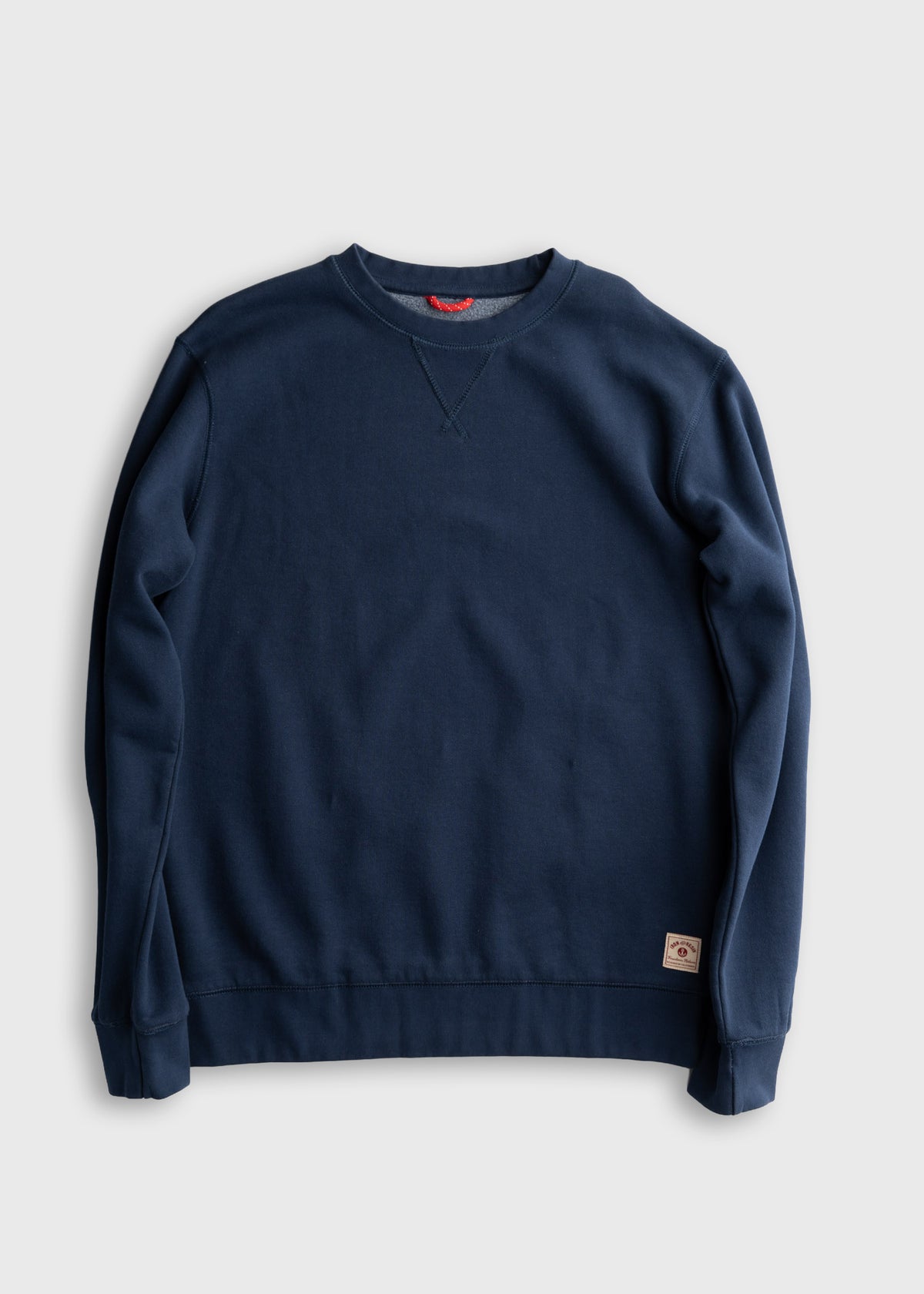 Navy blue crewneck sweatshirt with a small logo patch on the hem, laid flat on a light gray background.