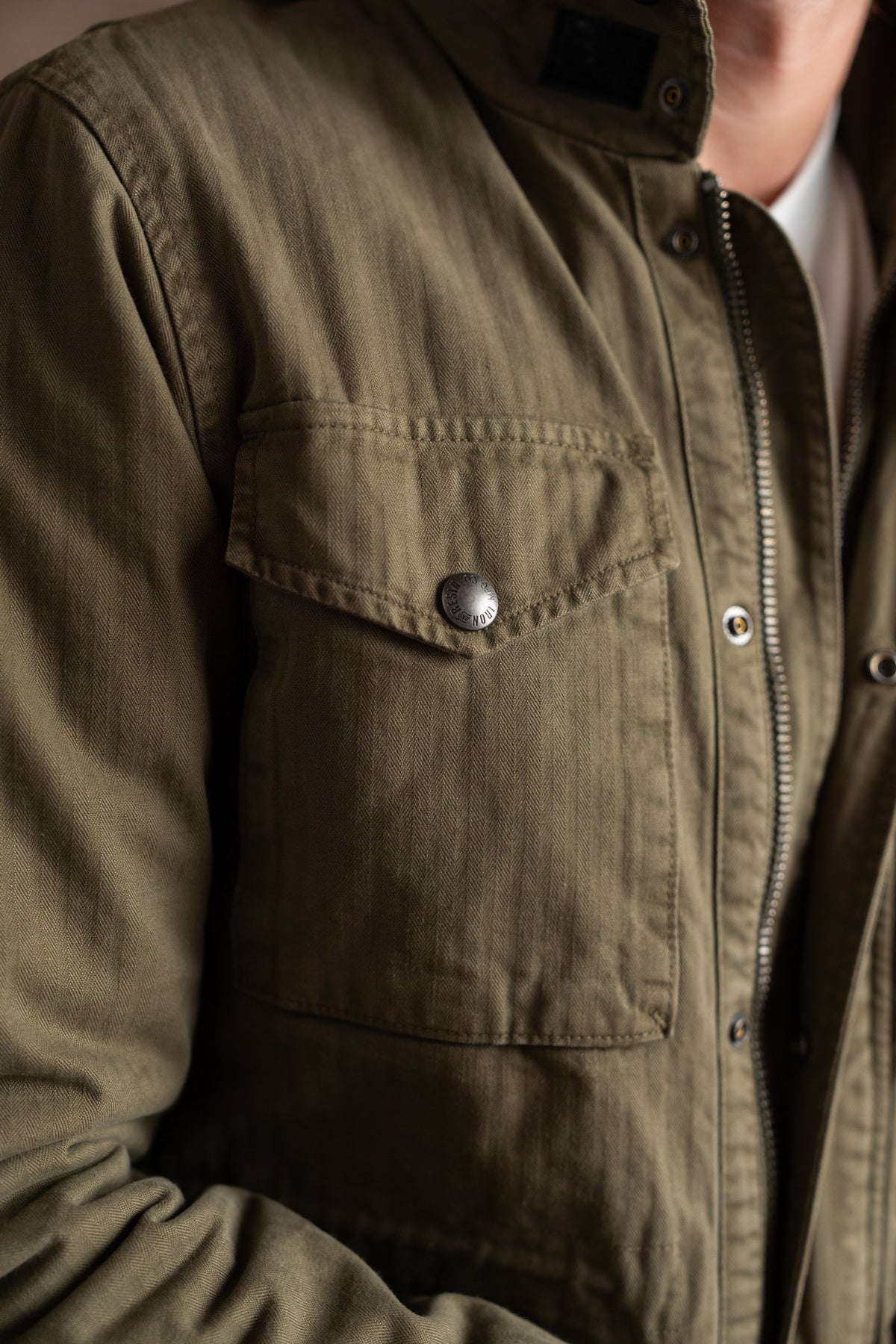 Close-up of a person wearing a green jacket with a buttoned pocket and zipper, highlighting the texture and design details.