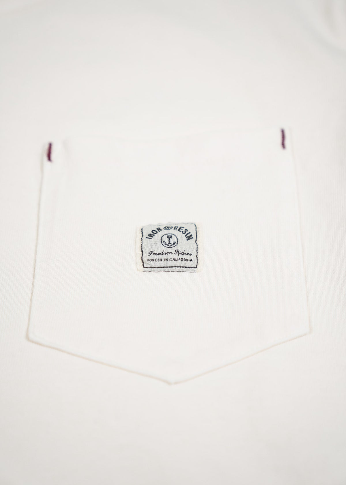 White shirt with a pocket featuring an "Iron and Resin" label, reading "Freedom Riders, Forged in California."