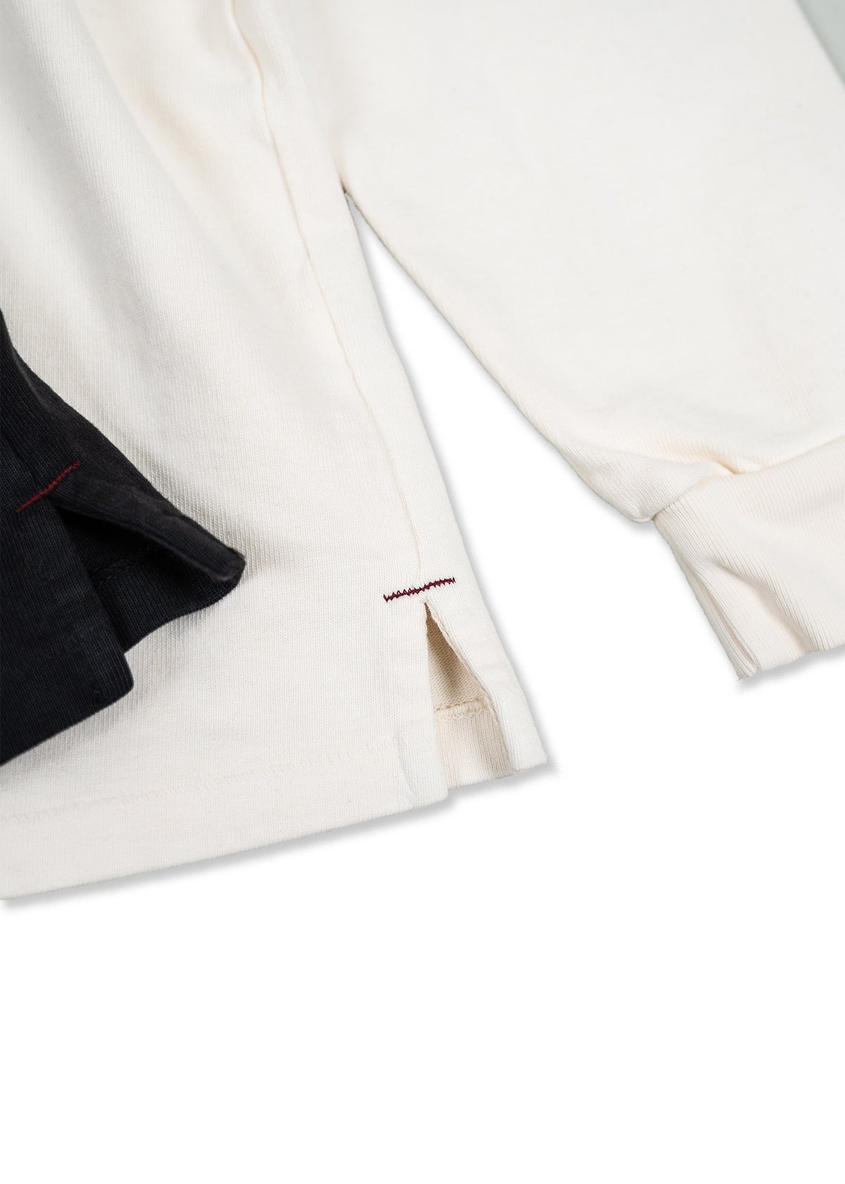 Close-up of cream and black ribbed shirts with red stitching, highlighting the fabric texture and side slit detail.