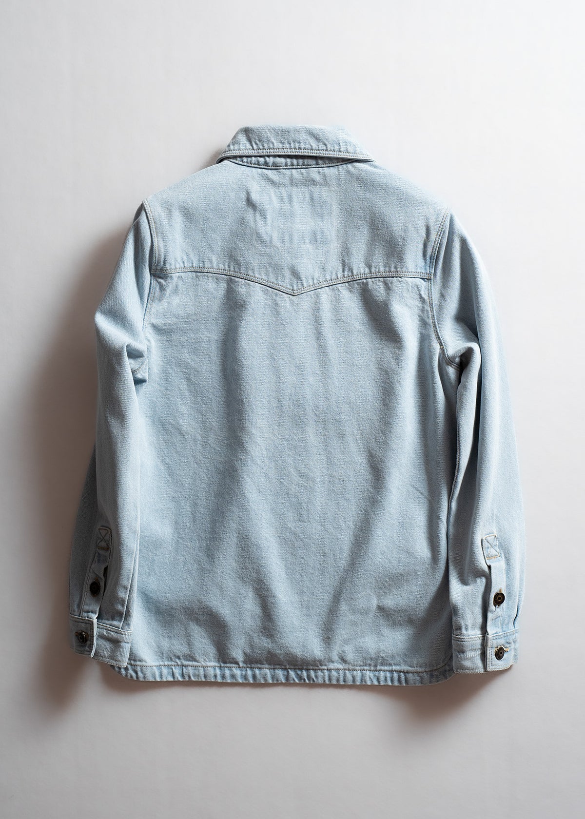 Back view of a light blue denim jacket with buttoned cuffs and a pointed yoke, displayed against a plain white background.