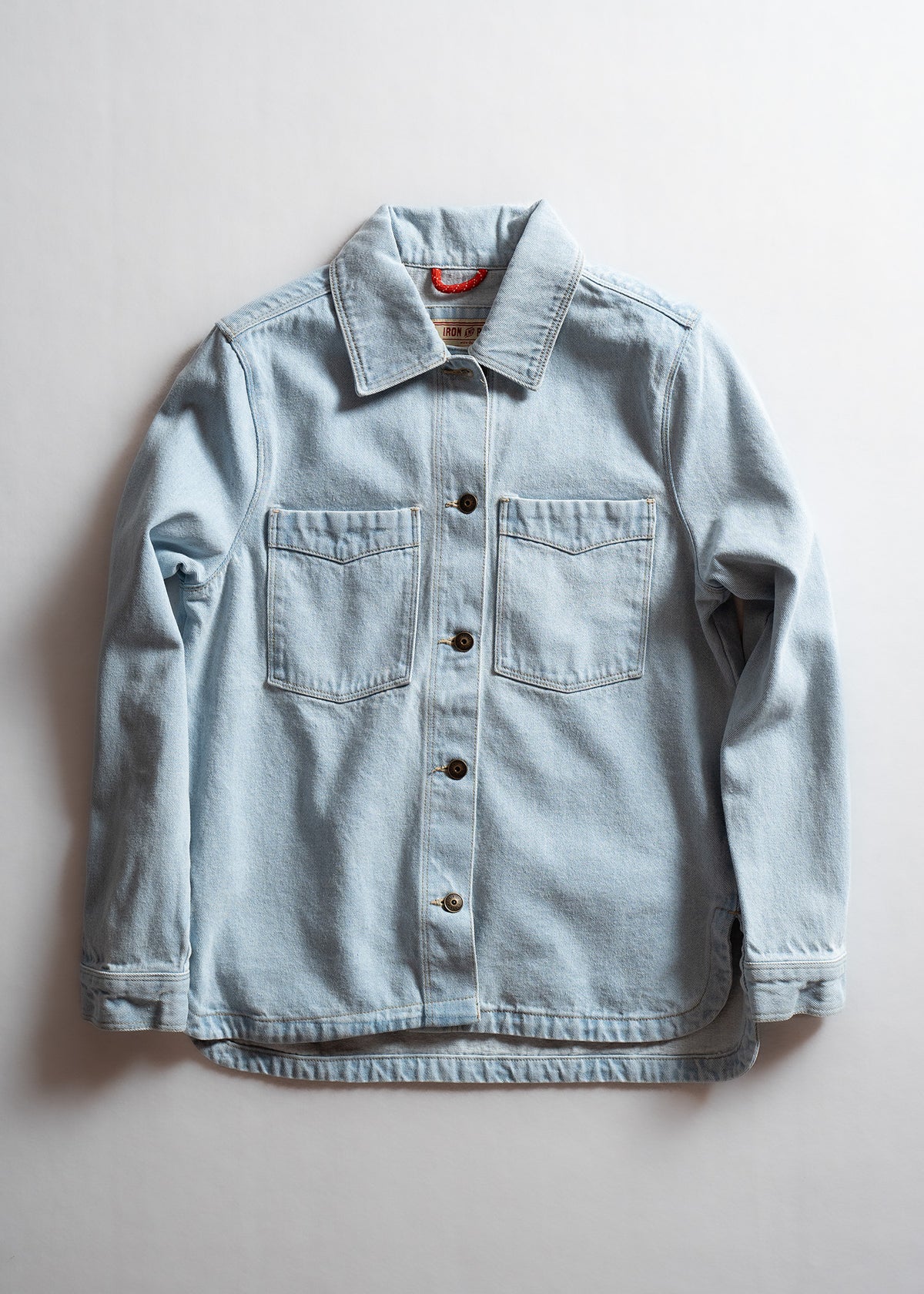 Light blue denim jacket with button closure and two chest pockets, laid flat on a white background.