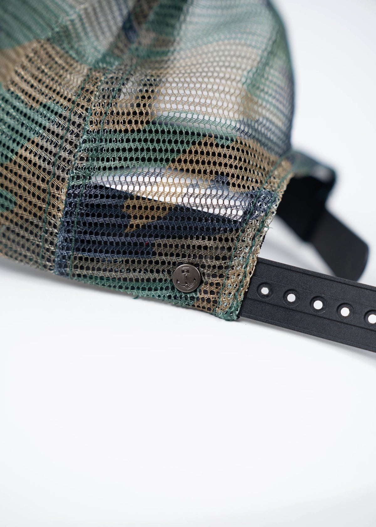 Close-up of a mesh trucker hat with adjustable black strap and button detail, showcasing its textured fabric and design.