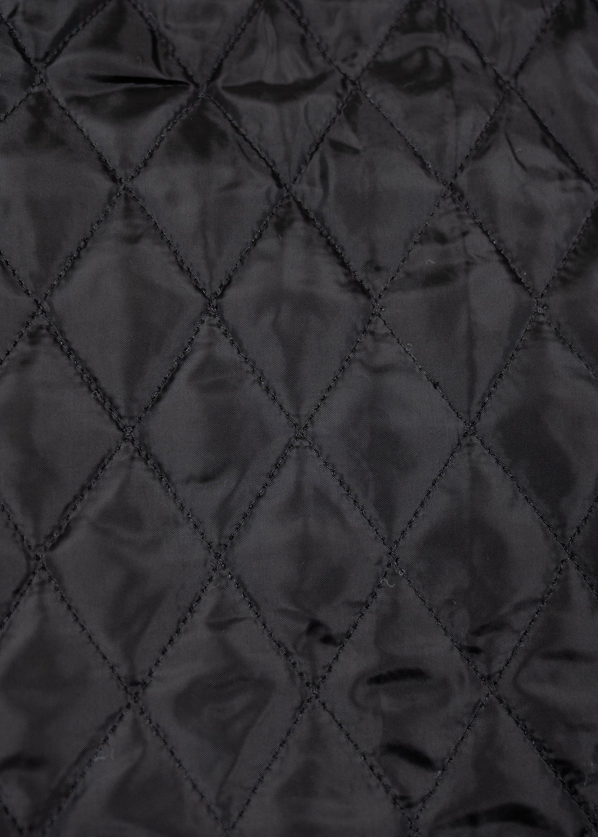 Close-up of black quilted fabric with diamond stitching pattern, creating a textured and elegant appearance.