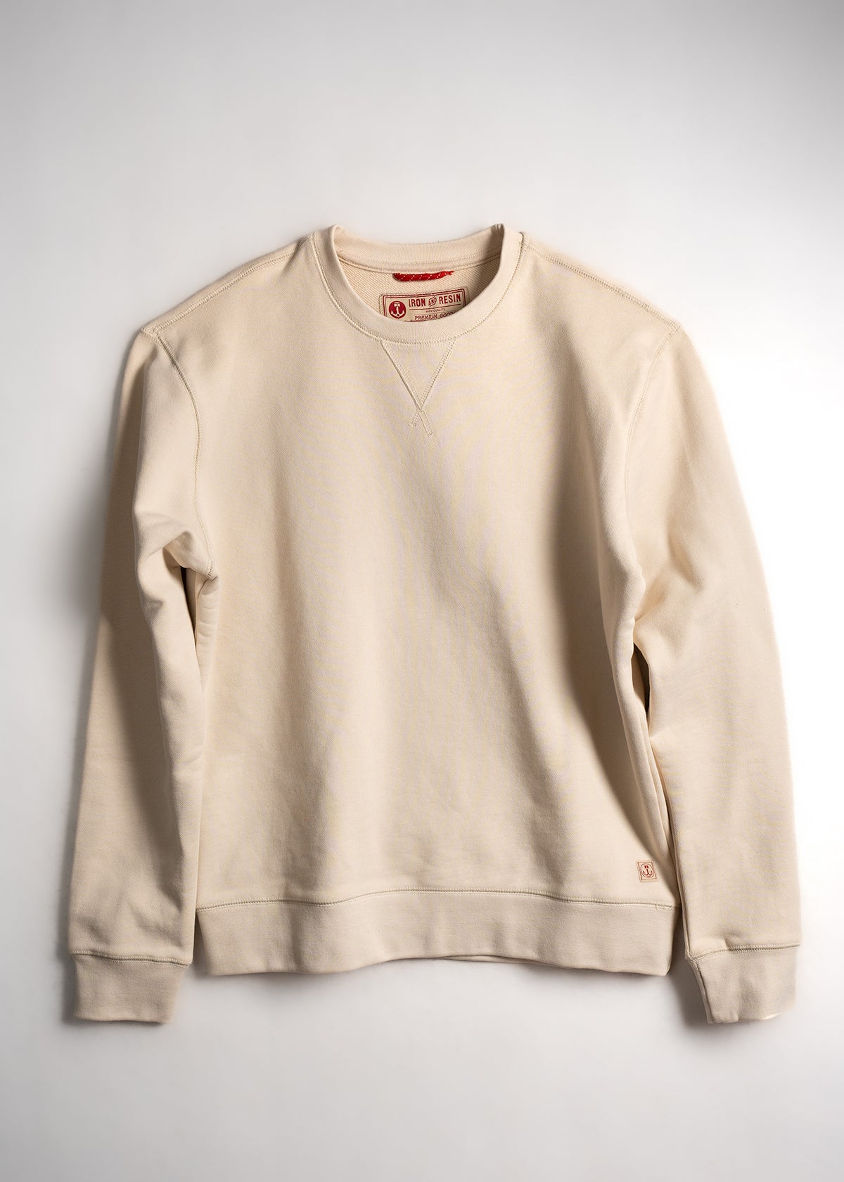 Cream crewneck sweatshirt with ribbed cuffs and hem, featuring a subtle V-stitch detail near the collar, laid flat on white.