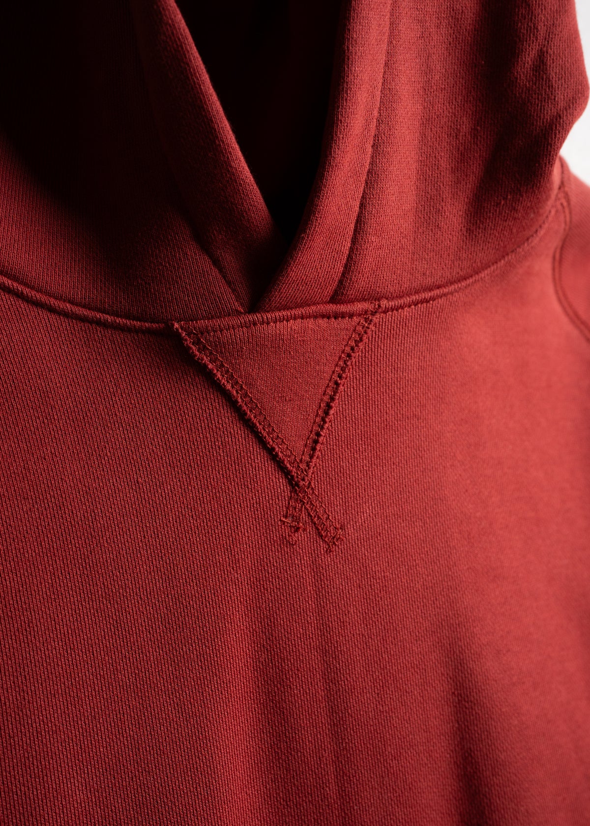 Close-up of a red hoodie showing detailed stitching and fabric texture, focusing on the neckline and hood area.