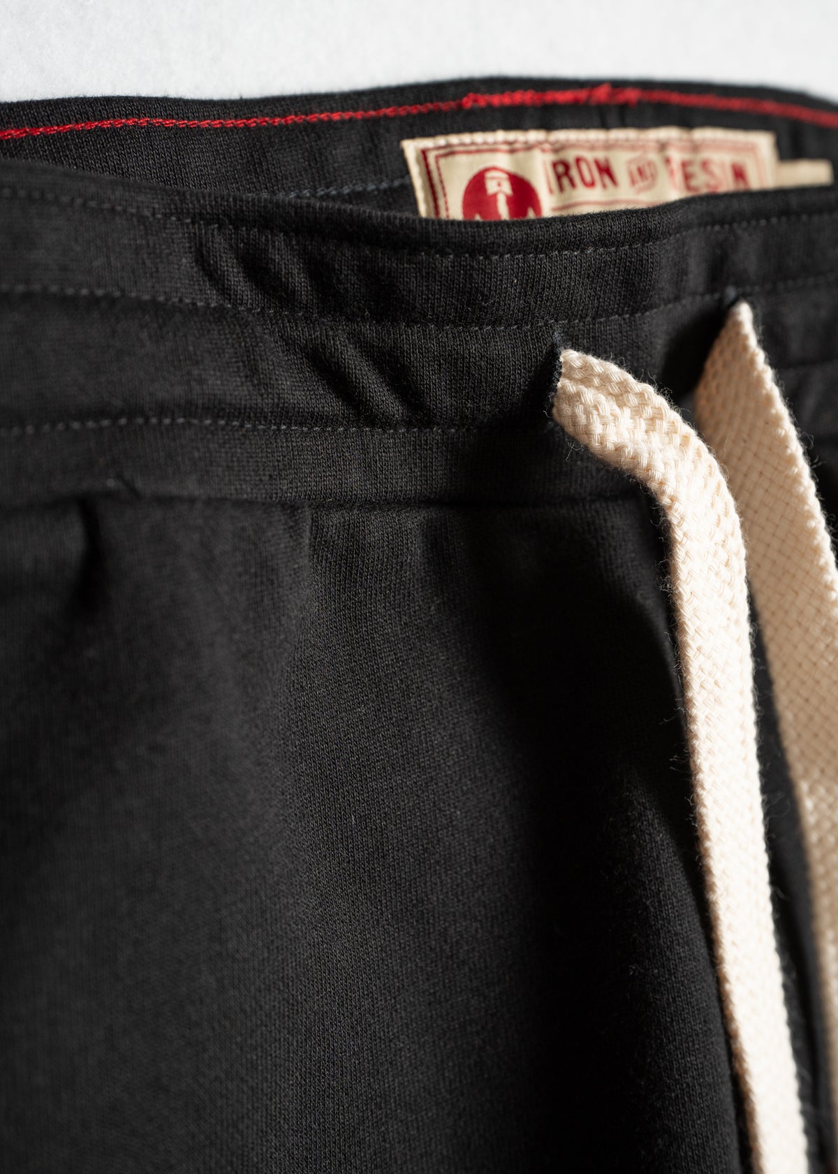 Close-up of black pants with cream drawstring and visible "Iron and Resin" label, highlighting texture and stitching details.