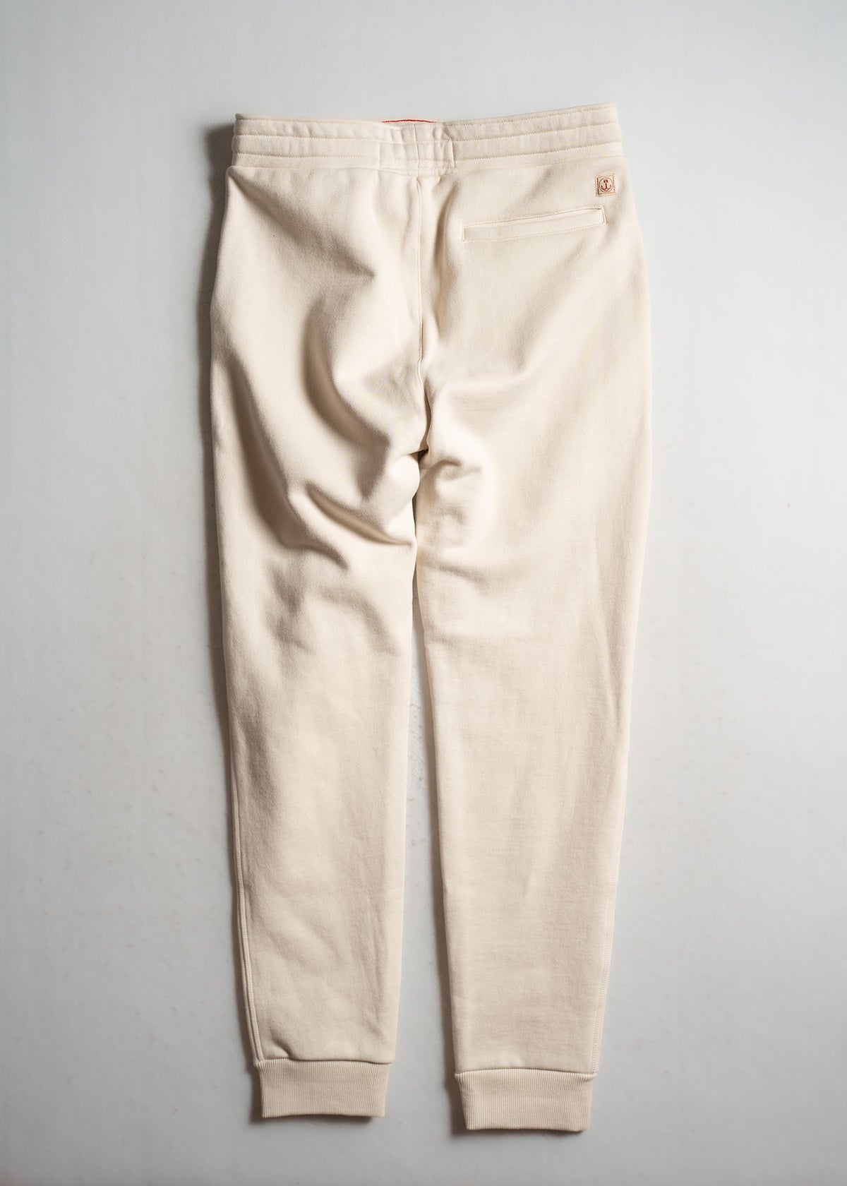 Beige sweatpants with a back pocket and elastic cuffs, laid flat on a light surface, showcasing casual and comfortable style.