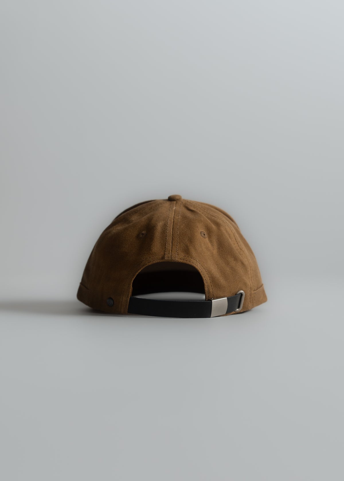 Brown baseball cap with black adjustable strap, viewed from the back, on a plain gray background. Minimalist and stylish design.