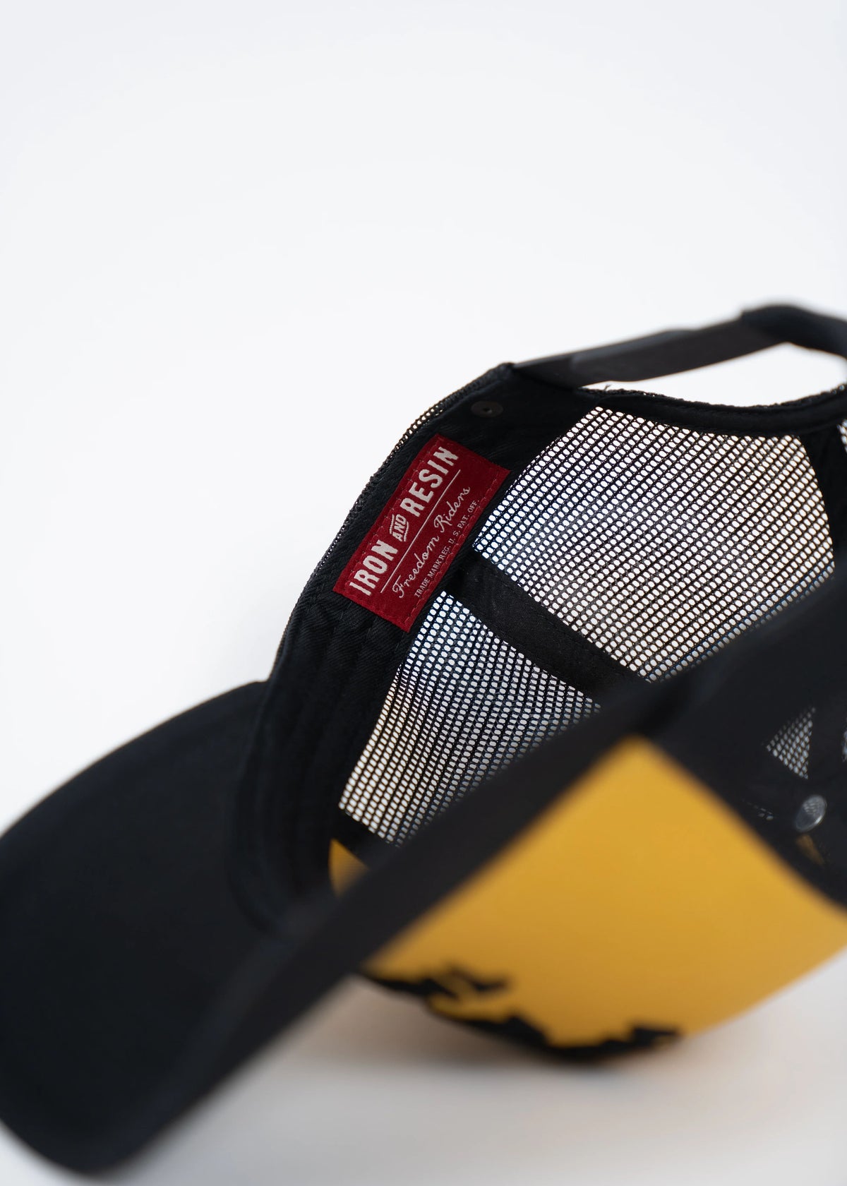 Black and yellow cap with mesh back, featuring an "Iron and Resin" label inside. The cap is partially open, showing its interior.