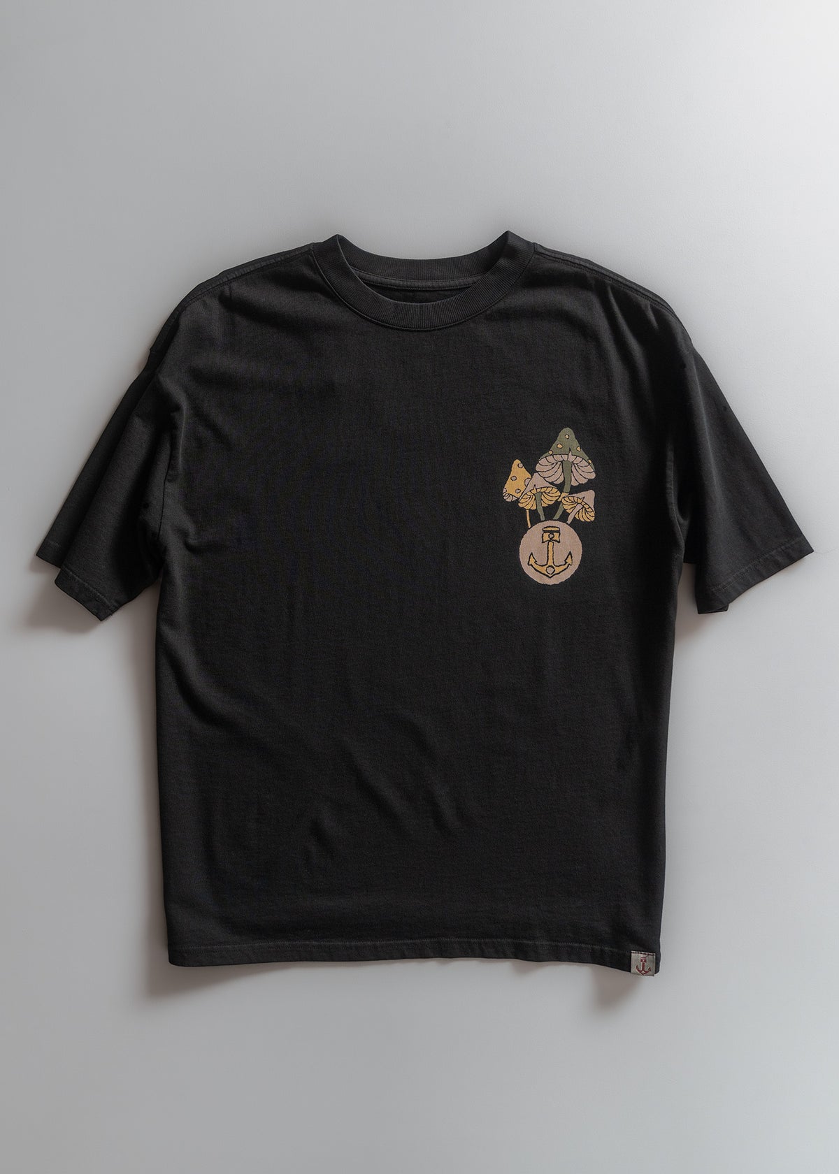 Black T-shirt with colorful mushroom and anchor design on the front, laid flat on a light gray background.