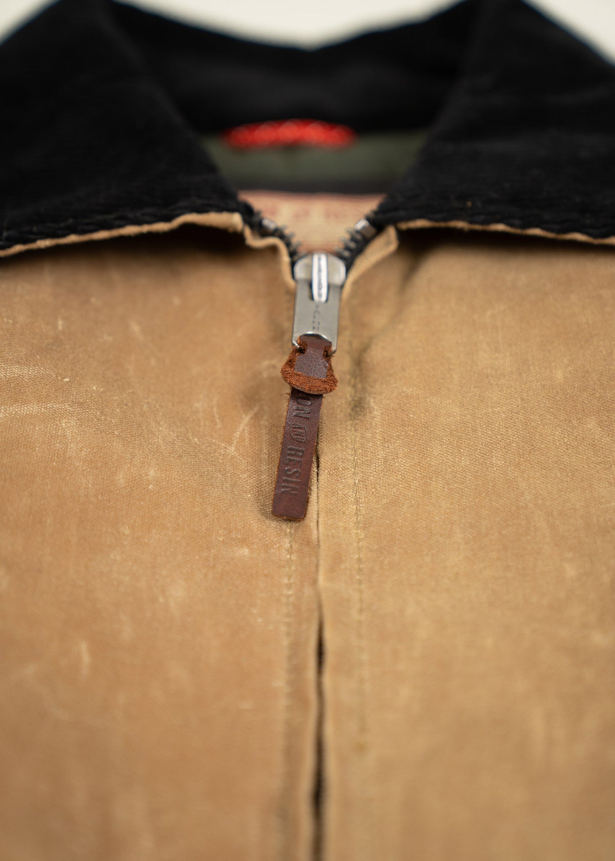 Close-up of a brown jacket with a black collar, featuring a metal zipper and leather pull tab, highlighting its rugged texture.