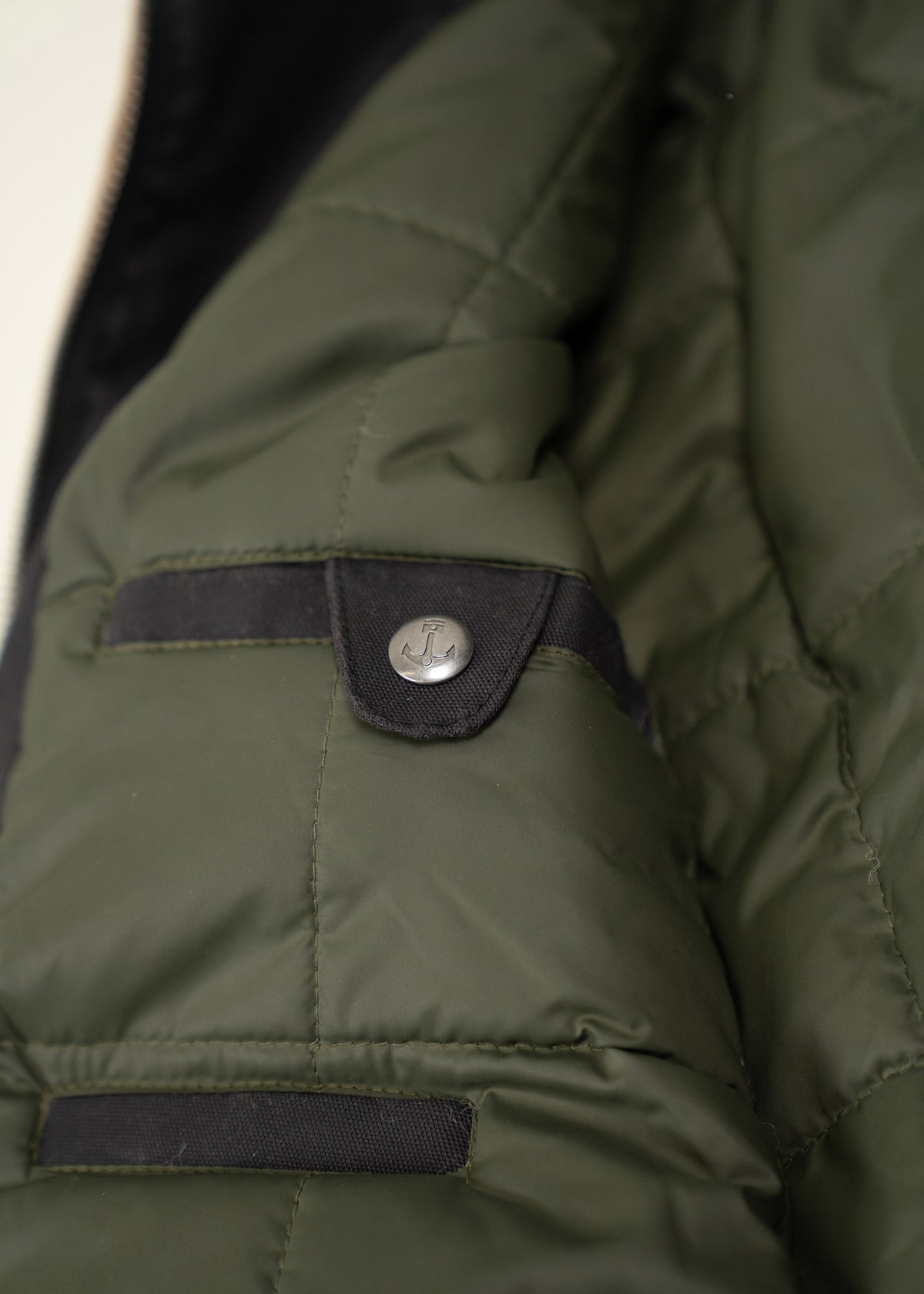 Close-up of a green quilted jacket with a black buttoned pocket flap, highlighting its textured fabric and stylish design.