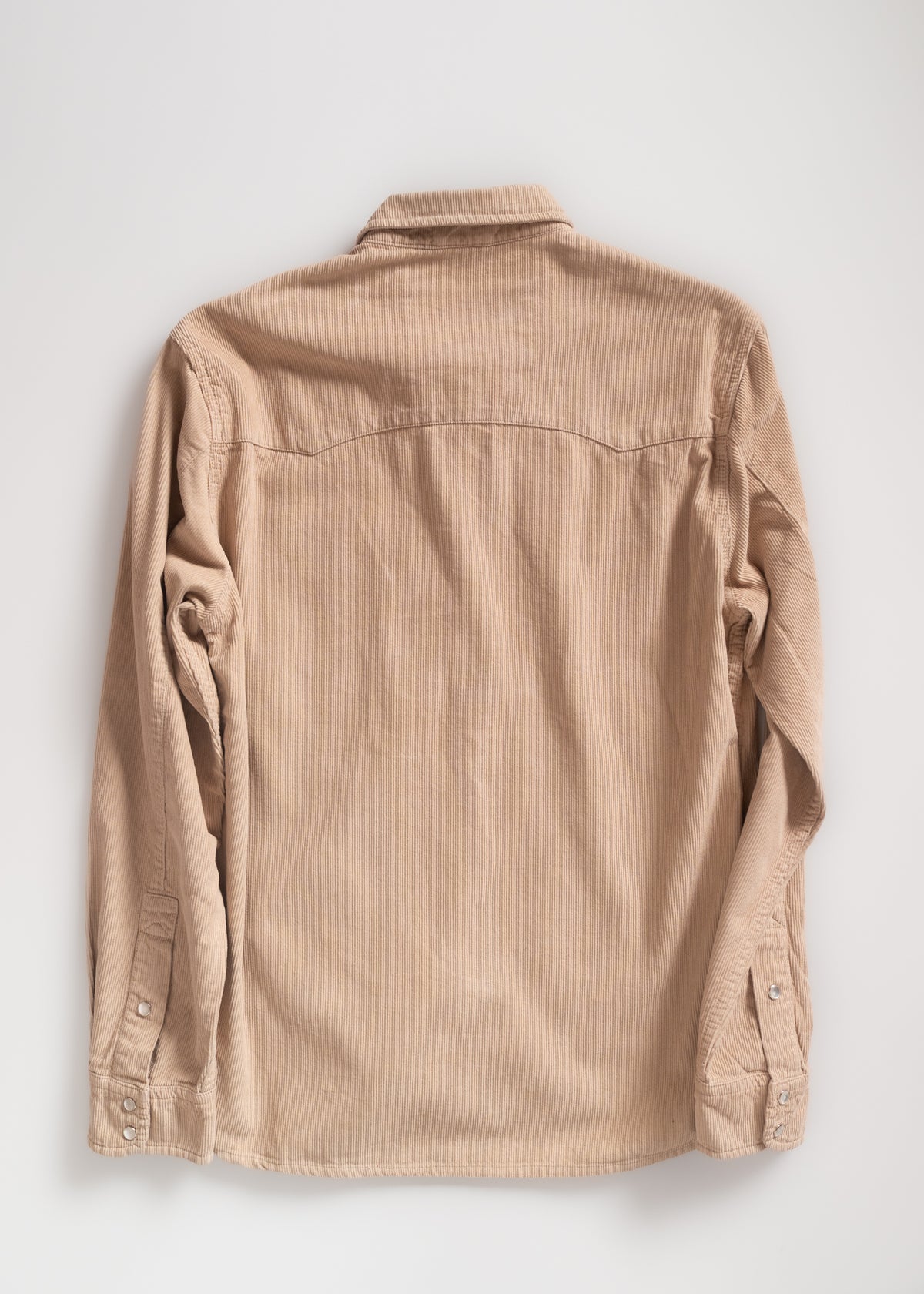 Beige corduroy shirt seen from the back, featuring long sleeves and buttoned cuffs, displayed on a plain white background.