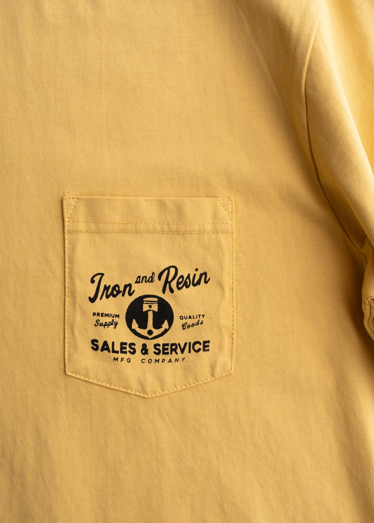 Yellow shirt with a pocket featuring "Iron and Resin" logo, "Sales & Service" text, and an anchor graphic, symbolizing quality.