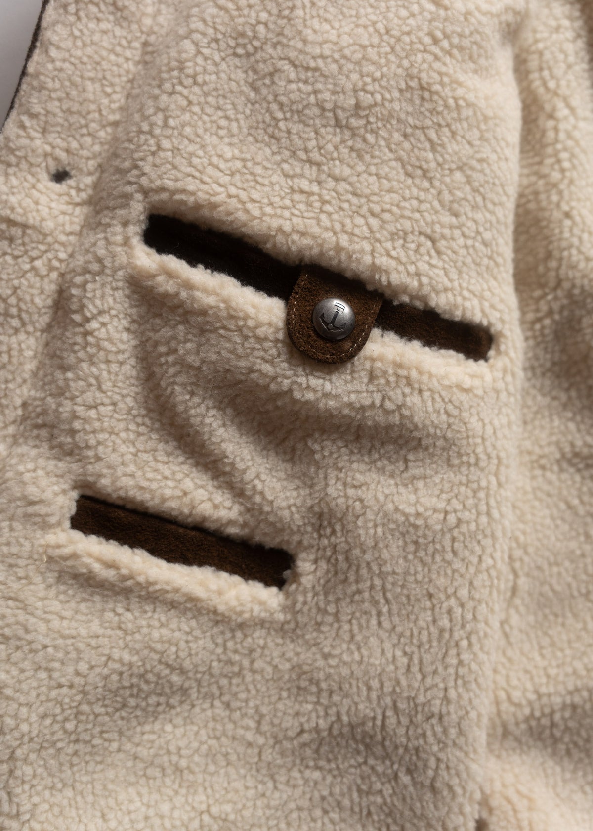 Close-up of a beige fleece jacket with two pockets and a metal button, showcasing its soft texture and cozy design.