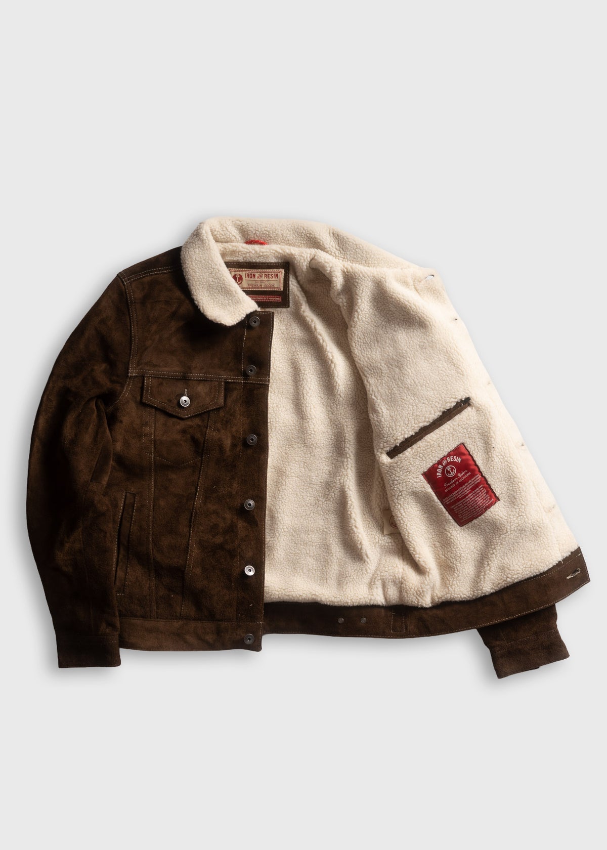 Brown suede jacket with white fleece lining, open to show interior label. Buttoned front and pocket detail visible.