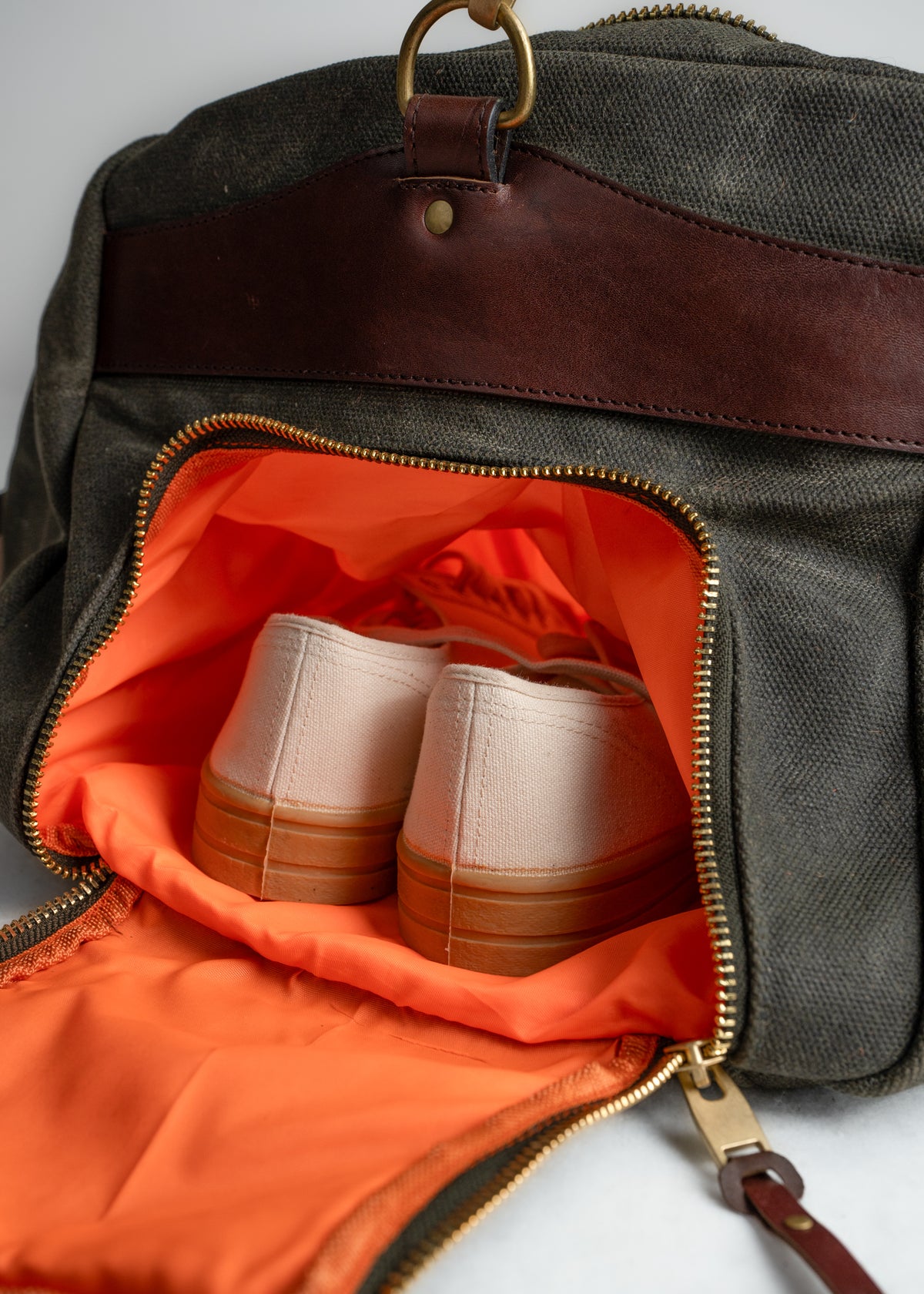 Canvas bag with leather accents, open to reveal white sneakers inside an orange-lined compartment, highlighting travel essentials.