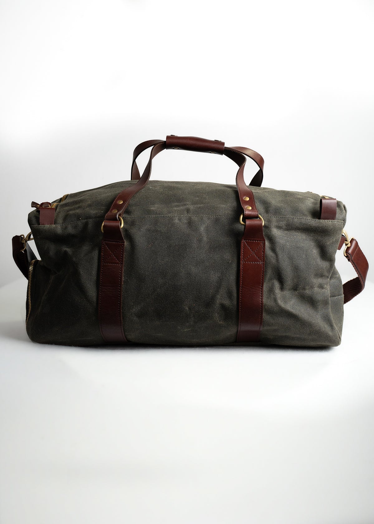 A large canvas duffel bag with brown leather straps and brass hardware, set against a plain white background.