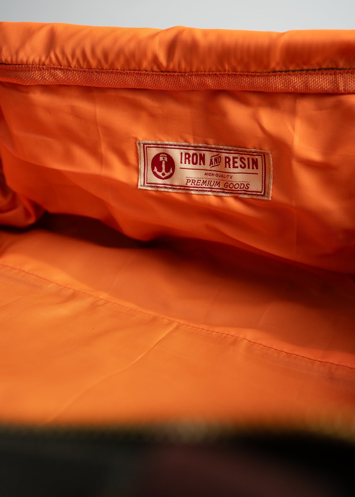 Orange jacket interior with "Iron and Resin" label, highlighting premium quality. The fabric appears smooth and well-crafted.