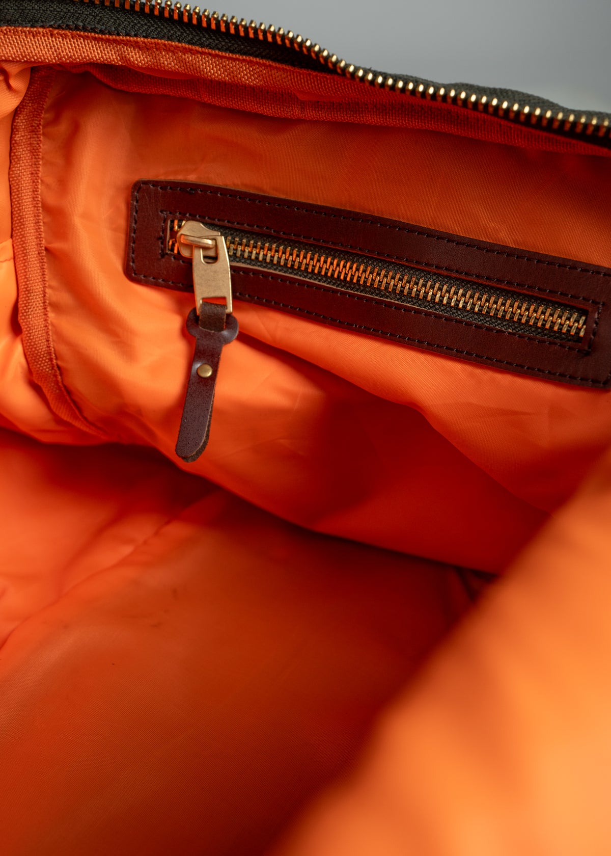 Orange bag interior with a brown leather zipper pocket and metal pull, showing detailed stitching and fabric texture.