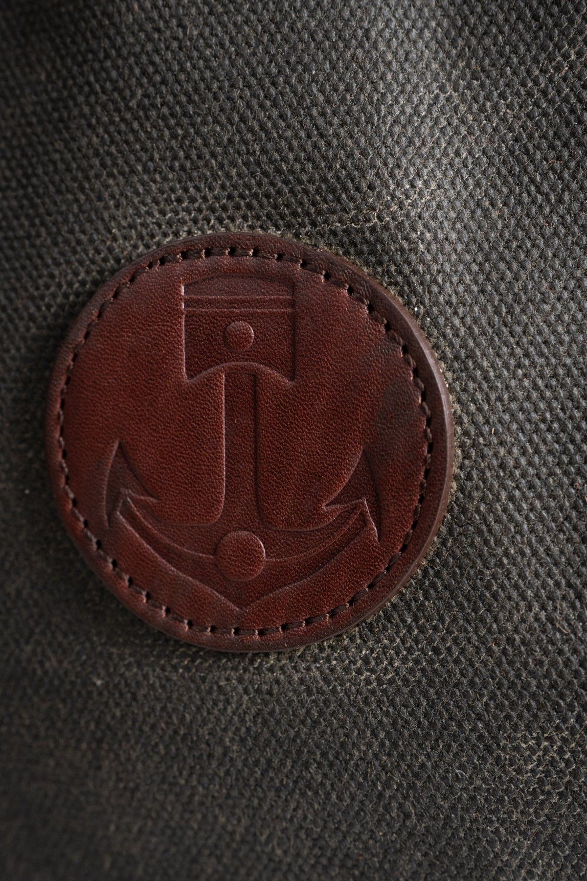 Brown leather patch with an anchor design on textured dark fabric, symbolizing nautical themes and craftsmanship.