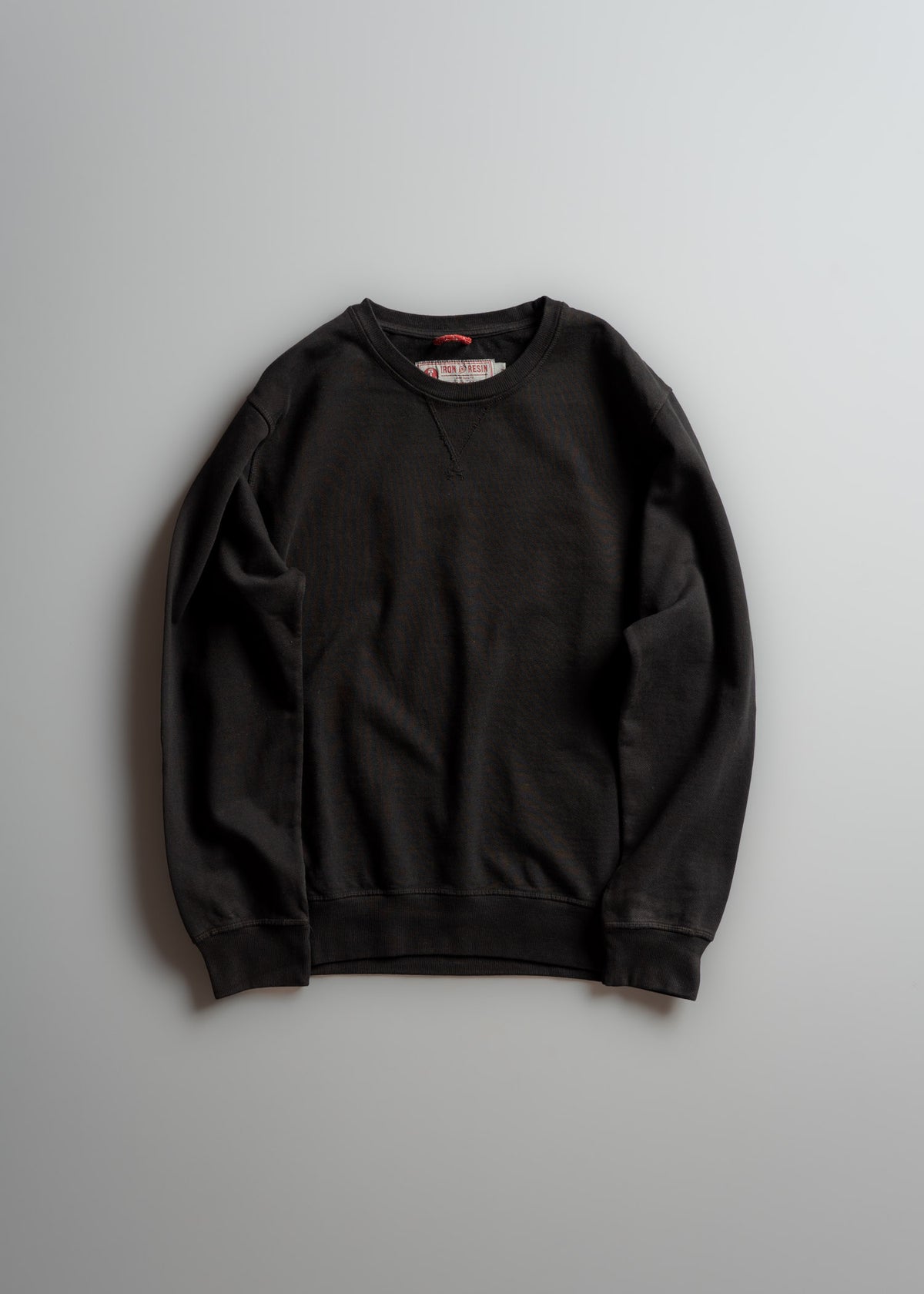 A black crewneck sweatshirt lies flat on a light gray surface, showcasing its simple design and casual style.