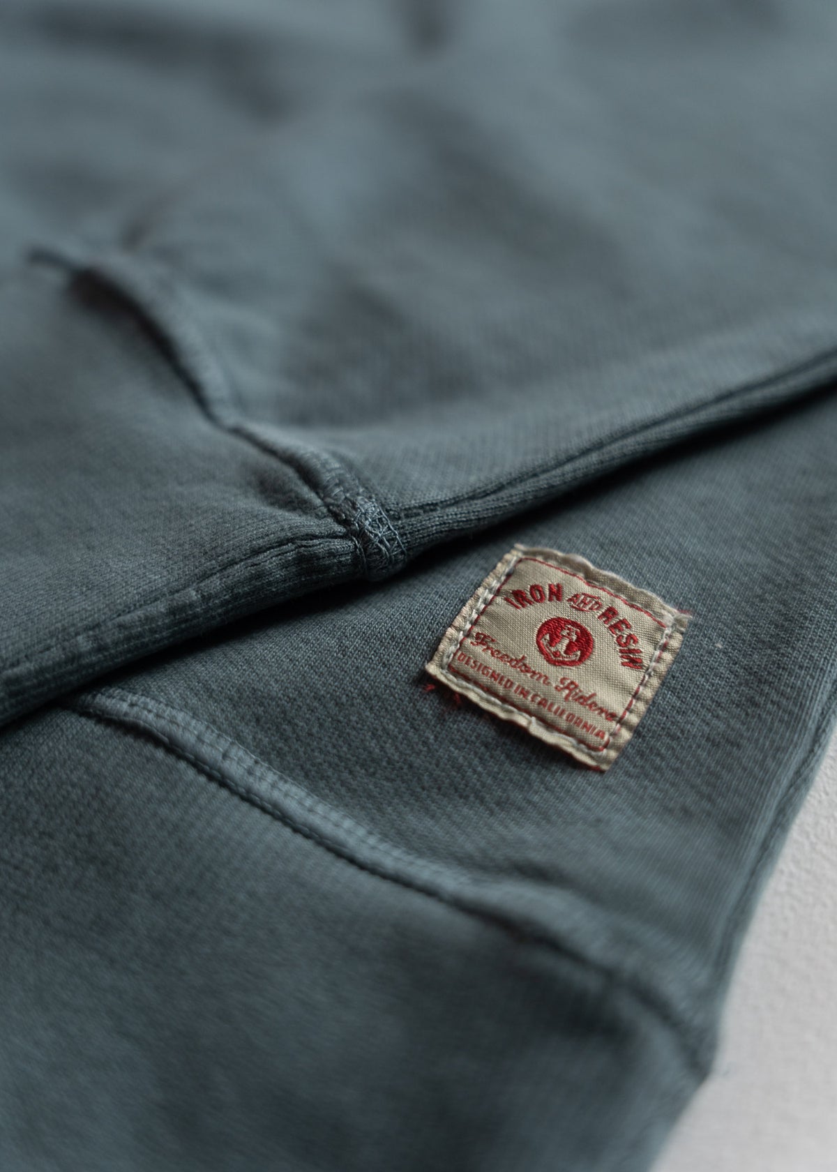 Close-up of a blue fabric with a vintage-style label reading "Iron and Resin, Designed in California" in red text.