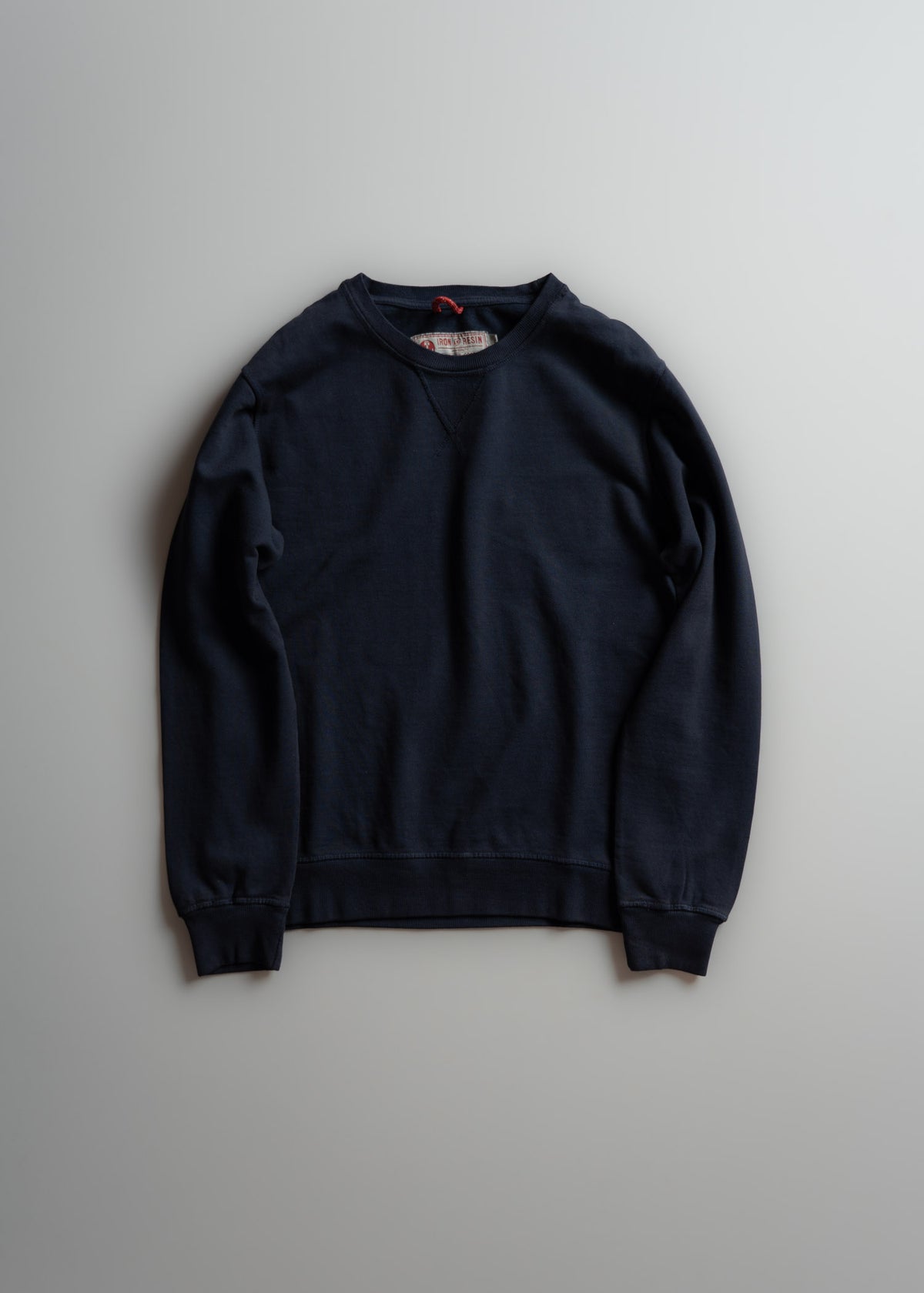 Navy blue crewneck sweatshirt with long sleeves, displayed on a light gray background, showcasing simple and classic design.