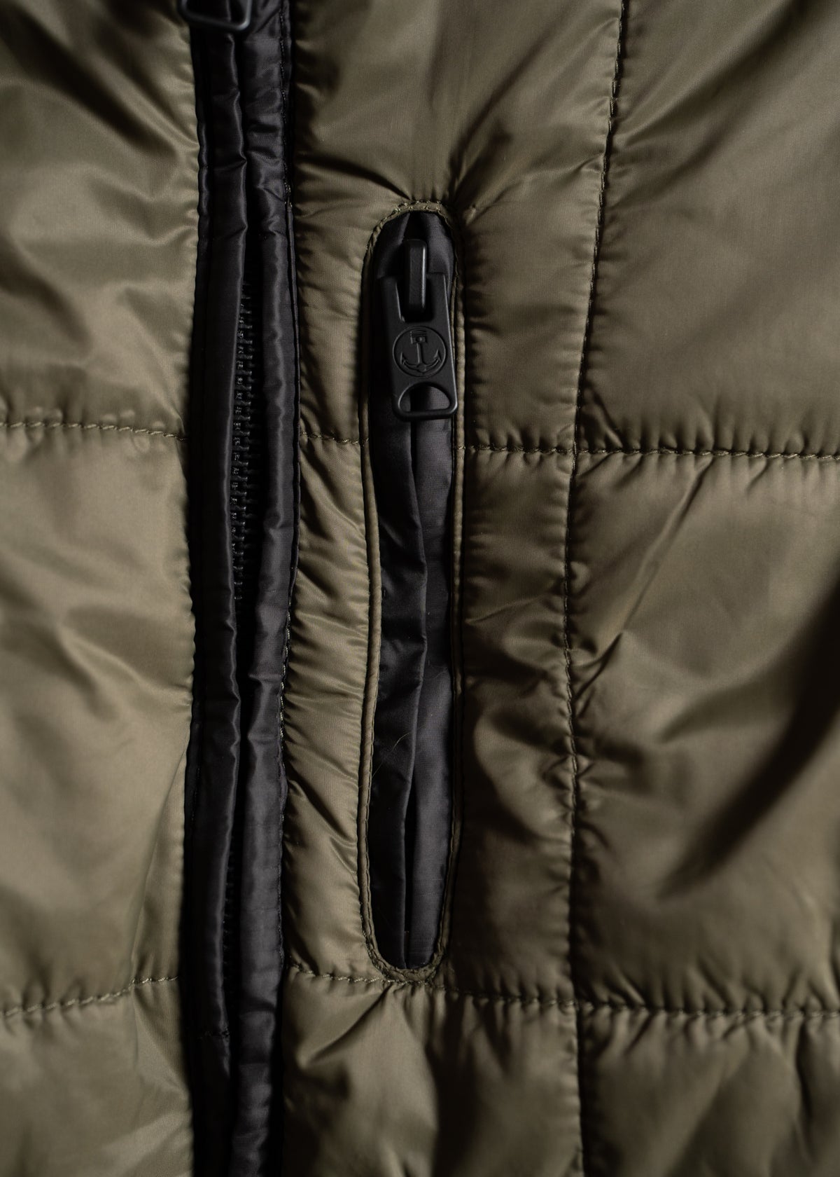 Close-up of a green quilted jacket with a black zipper and pocket, highlighting the texture and stitching details.