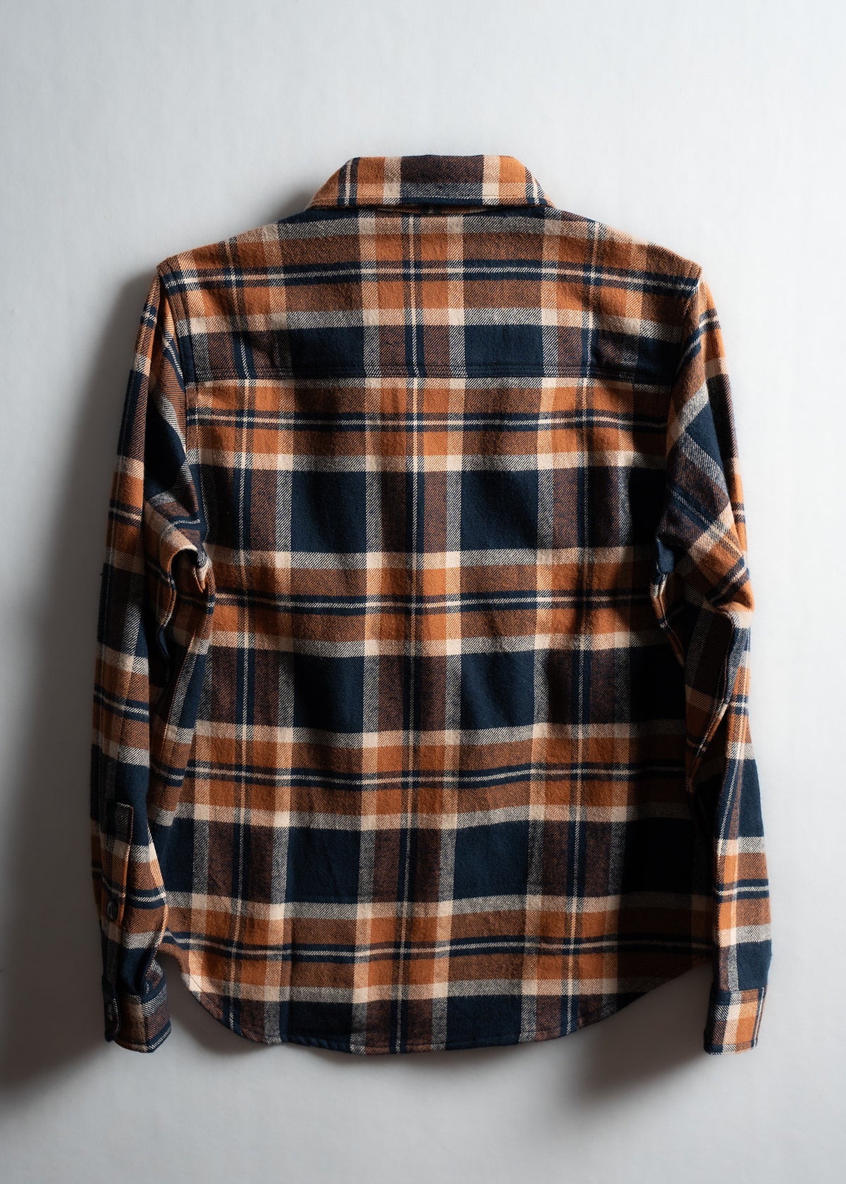 A plaid flannel shirt in orange and navy is laid flat on a white background, showcasing its back and checkered pattern.