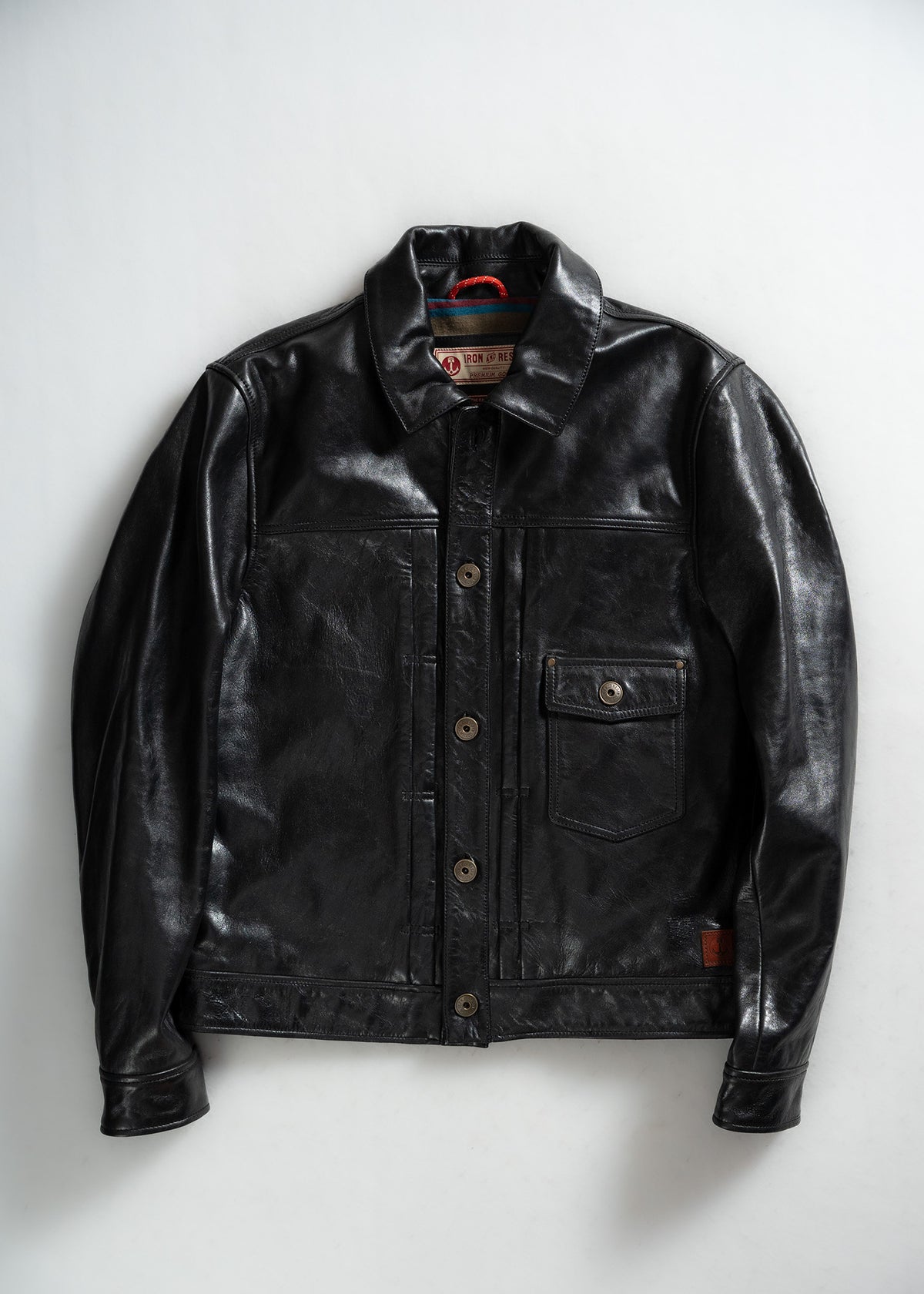 Black leather jacket with button closure and chest pocket, displayed on a light background, showcasing its sleek design and texture.