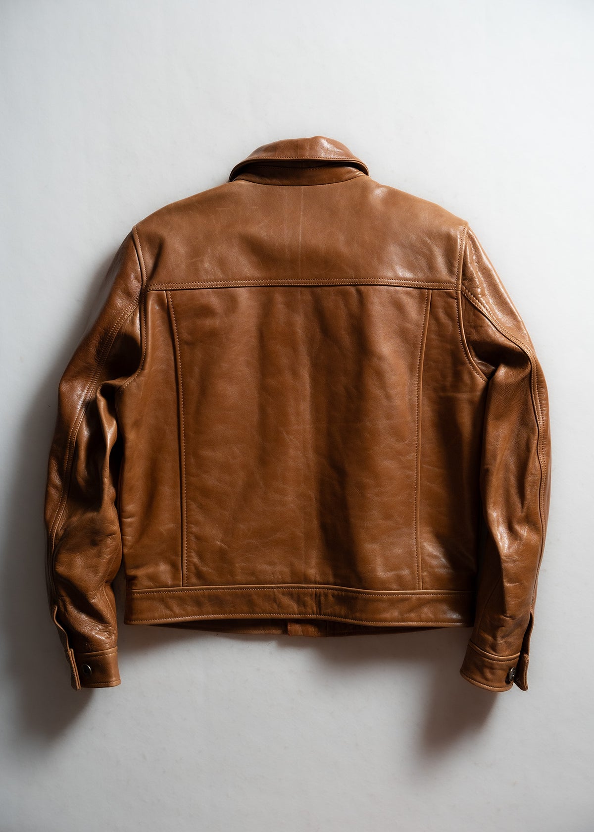 Brown leather jacket displayed on a white background, showcasing its back design and smooth texture.