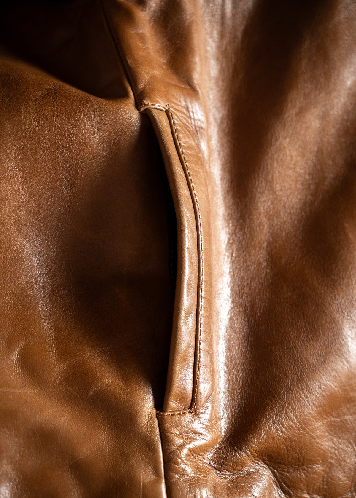 Close-up of a brown leather jacket pocket, highlighting the smooth texture and detailed stitching.