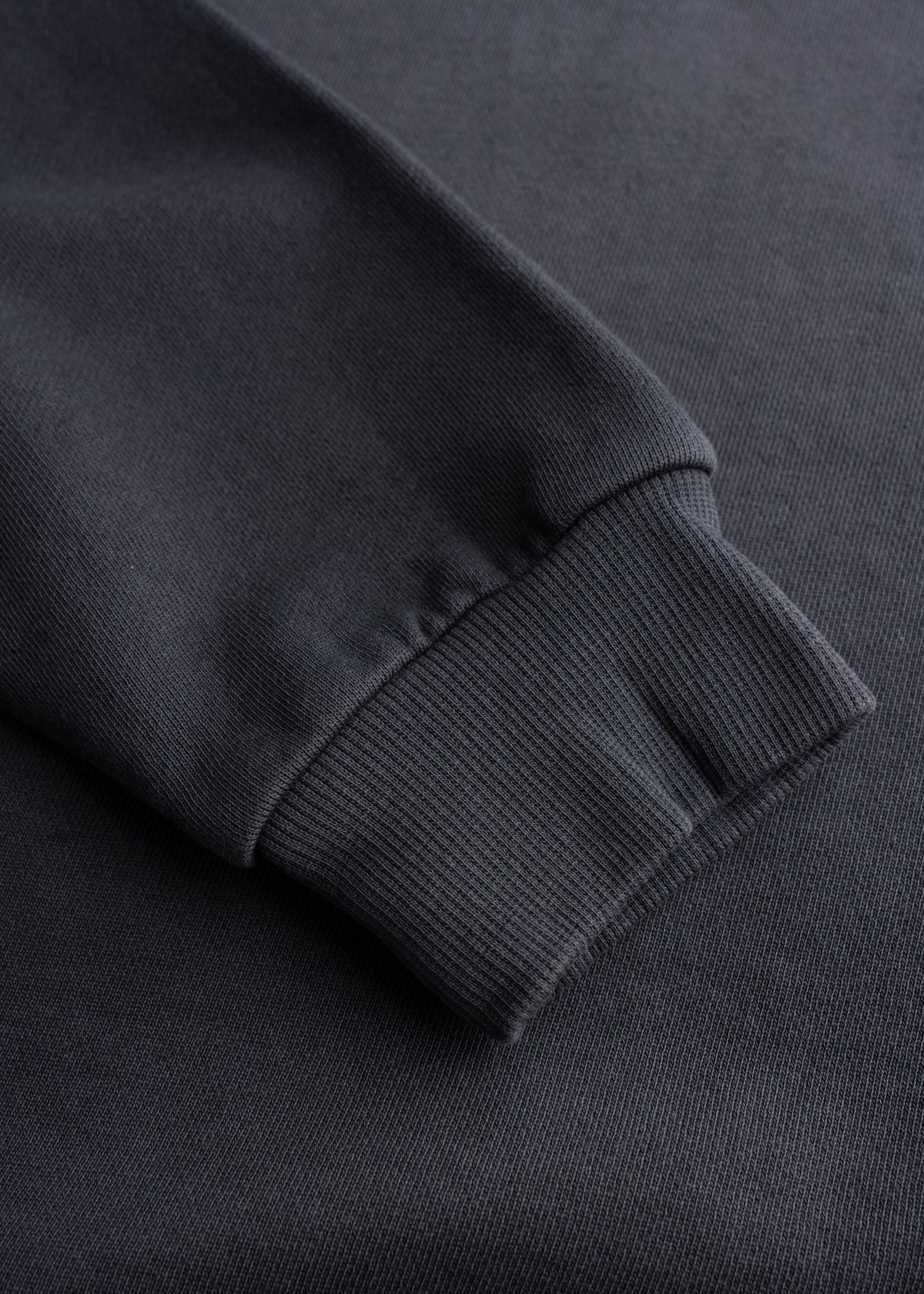 Close-up of a black sweatshirt sleeve with ribbed cuff, showcasing texture and fabric detail on a plain background.
