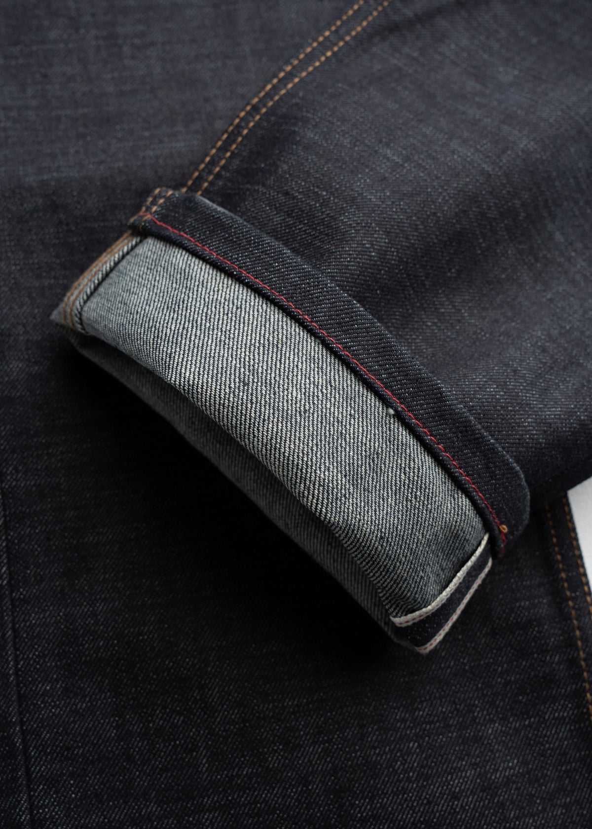 Close-up of dark denim jeans with a rolled cuff, highlighting the contrast stitching and texture of the fabric.