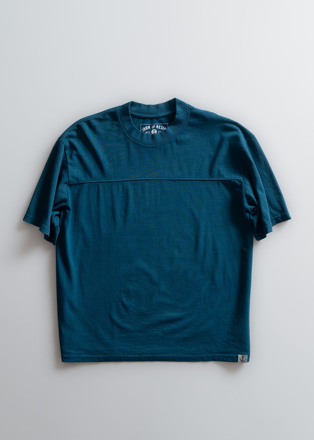 Teal blue T-shirt with short sleeves, crew neckline, and a small logo tag at the bottom. Simple, casual design on a light background.