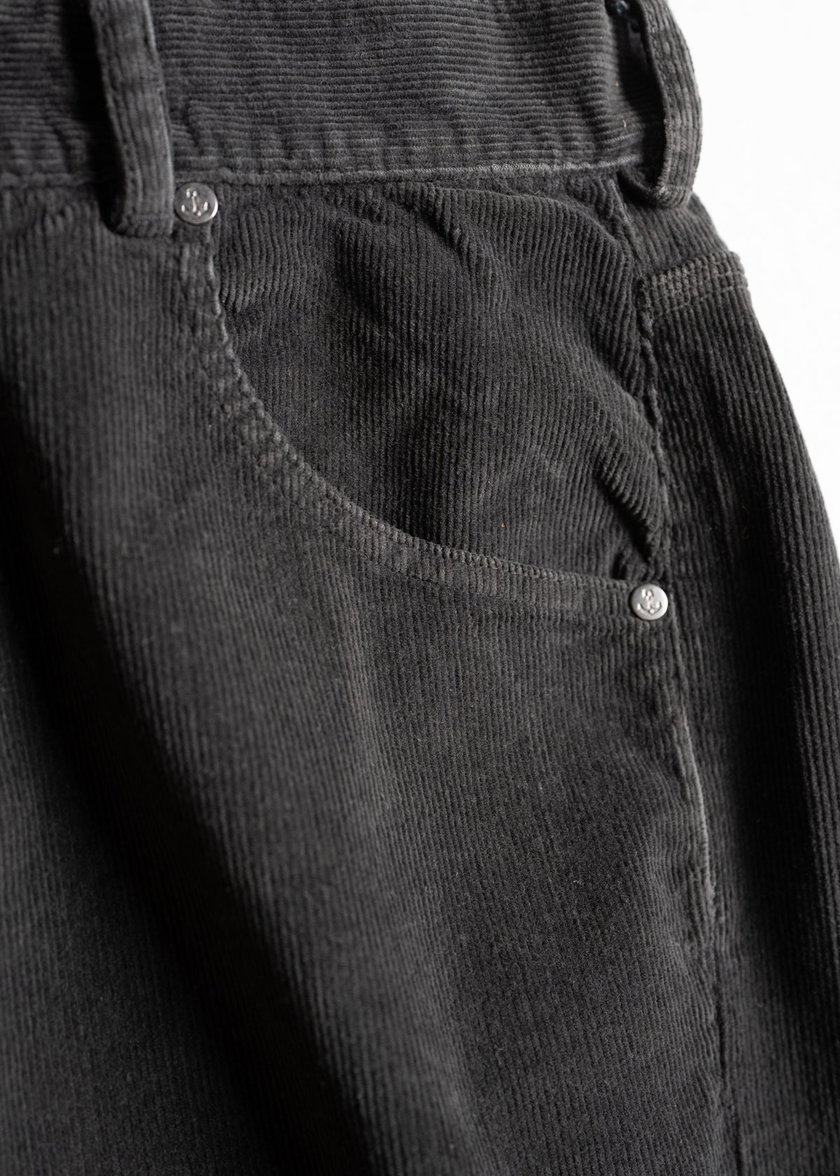 Close-up of black corduroy pants pocket with visible stitching and metal rivets, highlighting texture and fabric details.