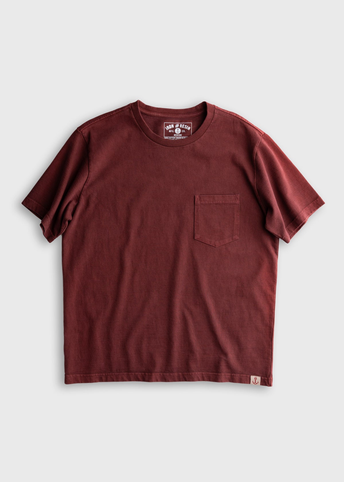 A maroon short-sleeve T-shirt with a chest pocket, displayed on a plain background, featuring a small logo tag at the hem.