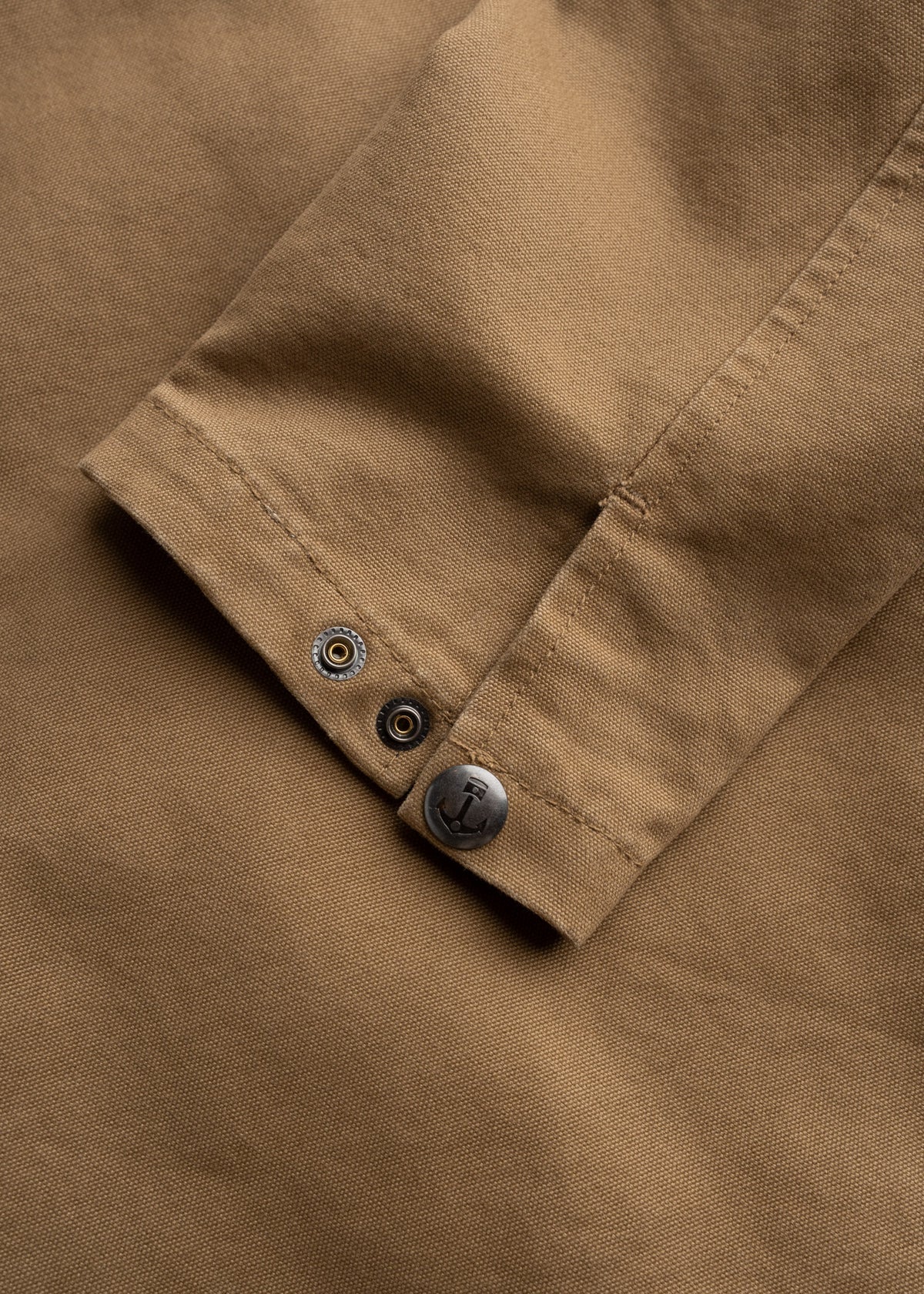 Close-up of a brown fabric sleeve with a metal button featuring an anchor design, highlighting the garment's detail and texture.