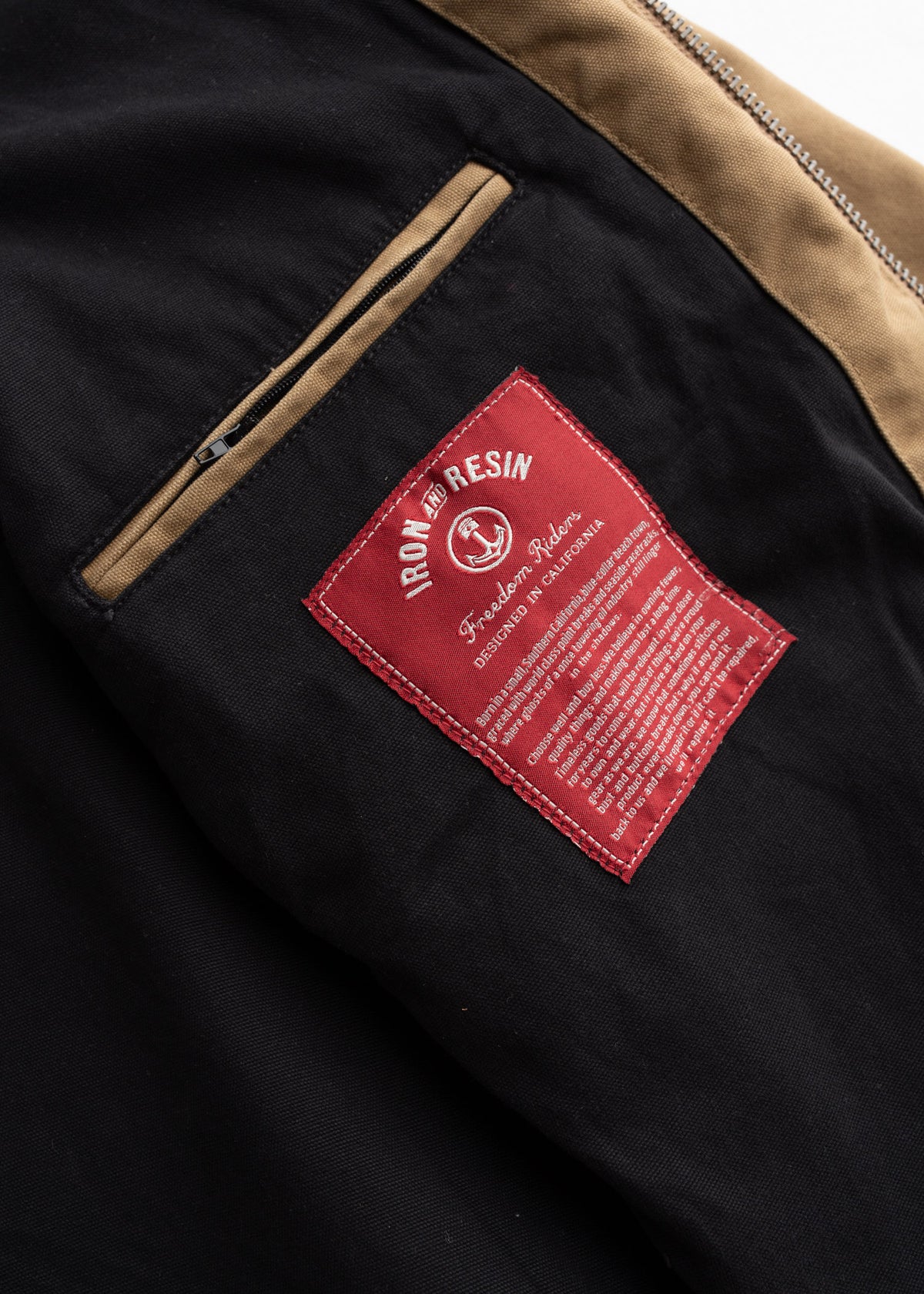 Close-up of a black jacket with a red Iron and Resin label and tan zipper detailing, highlighting the brand's craftsmanship.